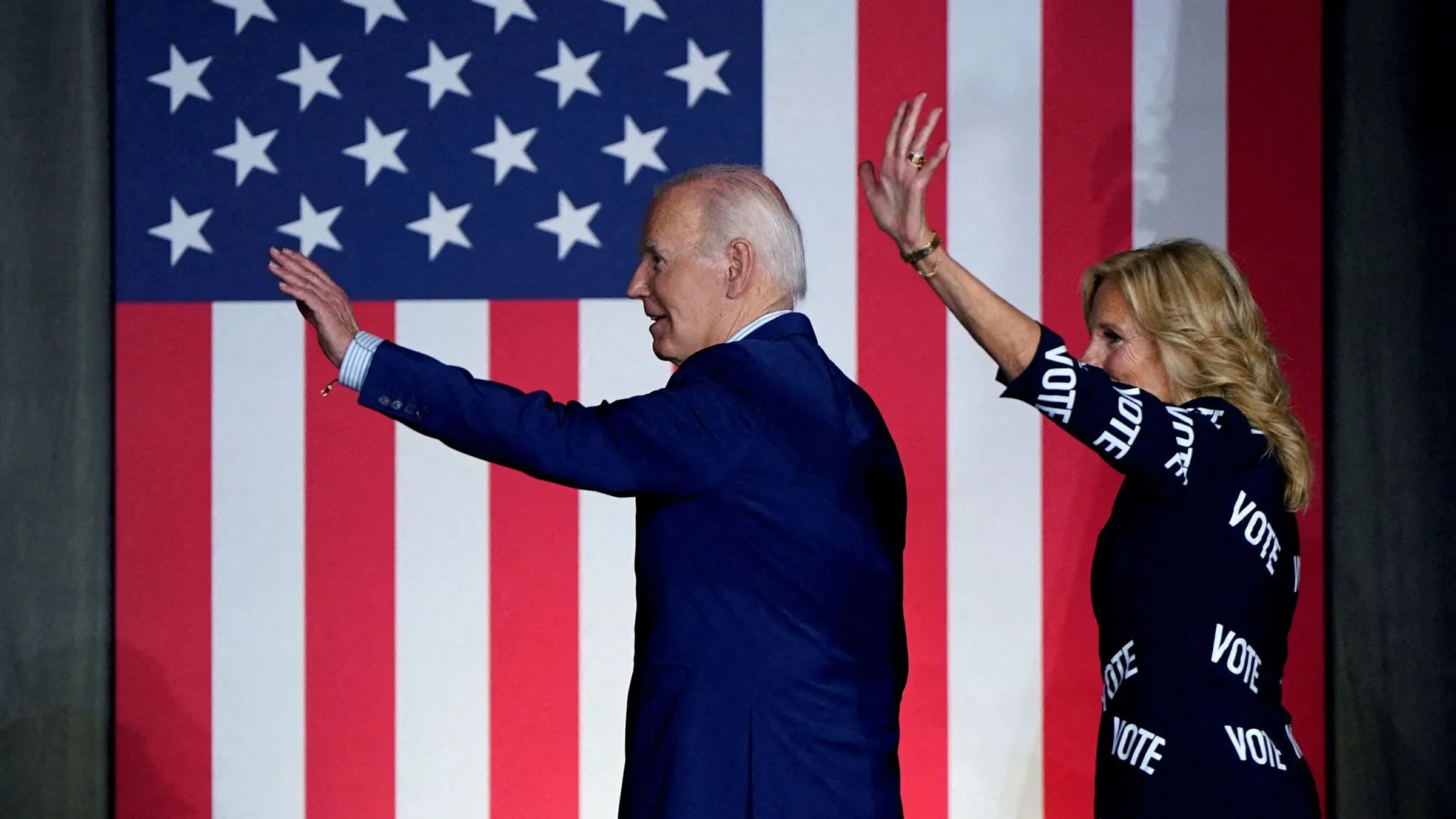 جيل بايدن وجو بايدن يلوحان للجمهور أمام علم الولايات المتحدة، معبرين عن الدعم في سياق الانتخابات.