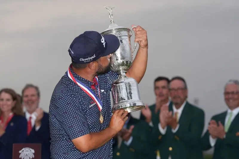 سباون يحتفل بفوزه بكأس بطولة الولايات المتحدة المفتوحة، ممسكًا بالكأس بينما يصفق الجمهور خلفه.