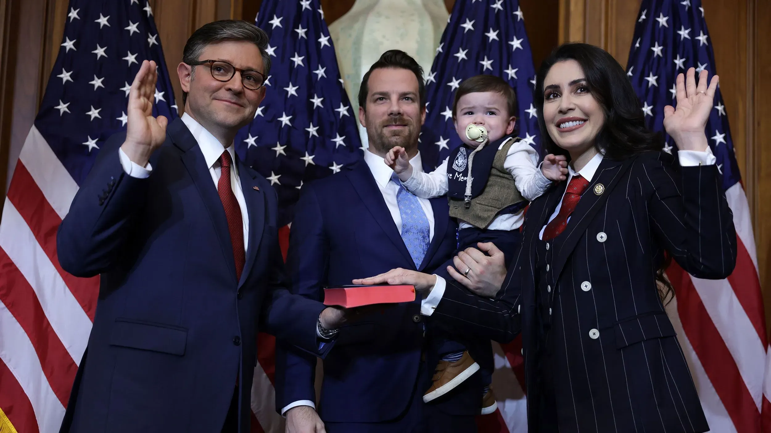 النائب آنا باولينا لونا تحمل طفلًا بينما تشارك في مراسم رسمية مع زملائها في مجلس النواب الأمريكي، مع العلم الأمريكي في الخلفية.