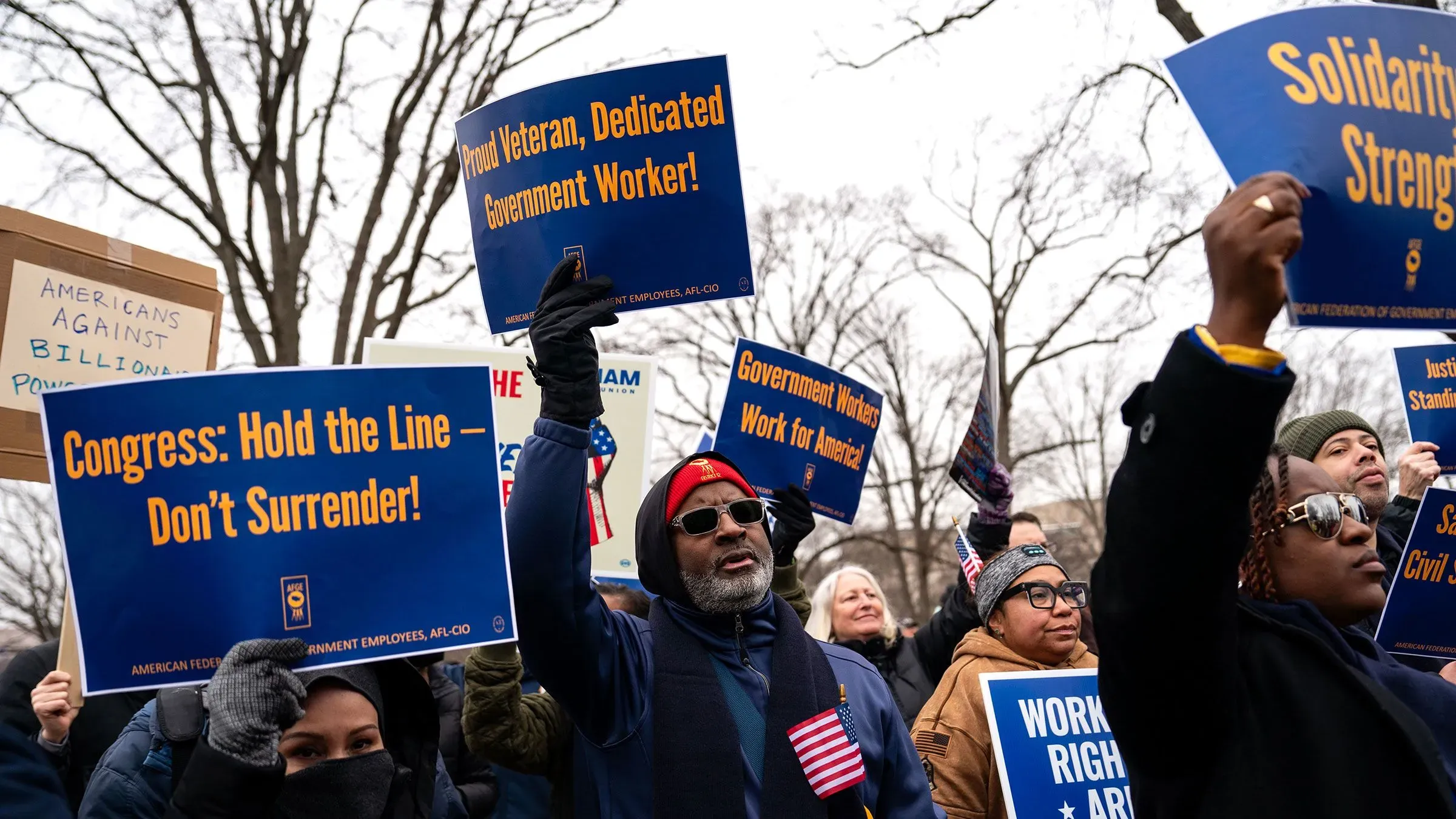 محتجون يحملون لافتات تدعو إلى دعم موظفي الحكومة ومنع الإقالات الجماعية، خلال تظاهرة أمام مبنى حكومي.