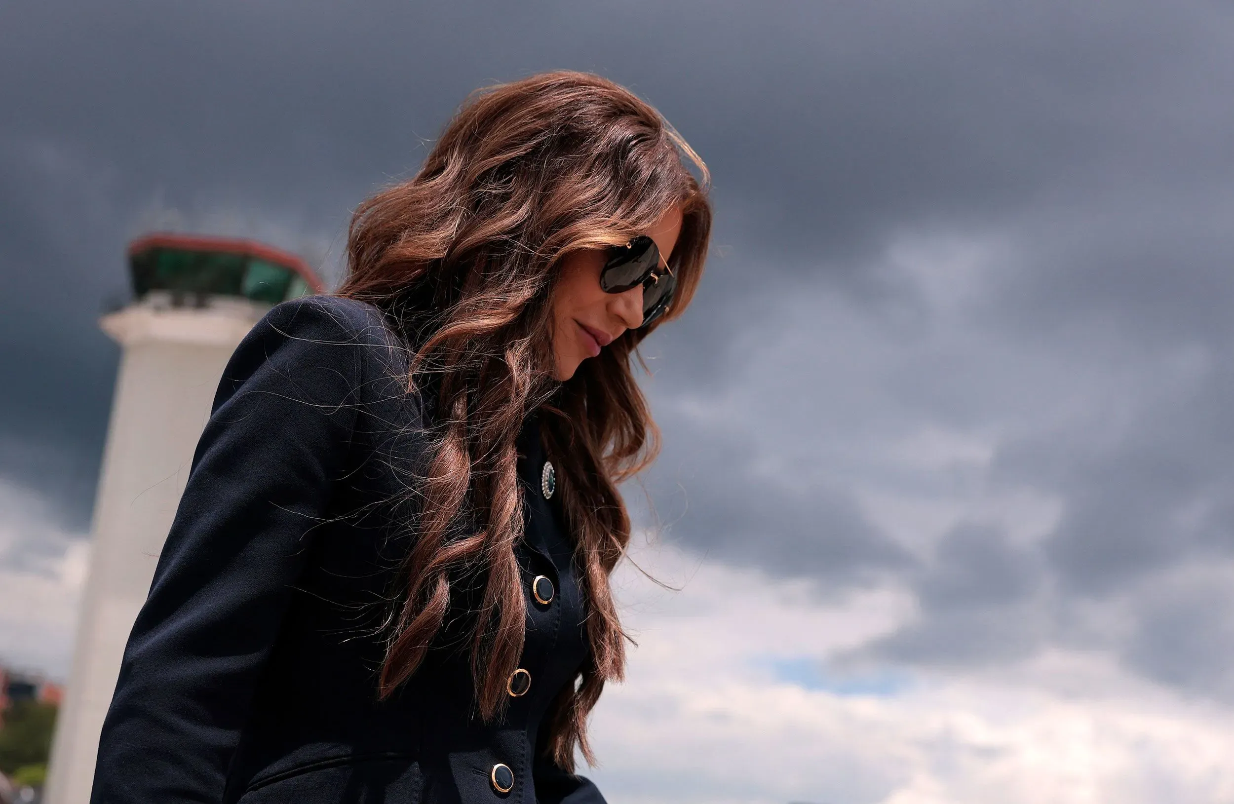 امرأة ترتدي نظارات شمسية وتظهر بمظهر جاد، تسير تحت سماء غائمة، مما يعكس أجواء التوتر المرتبطة بقضية قانونية.