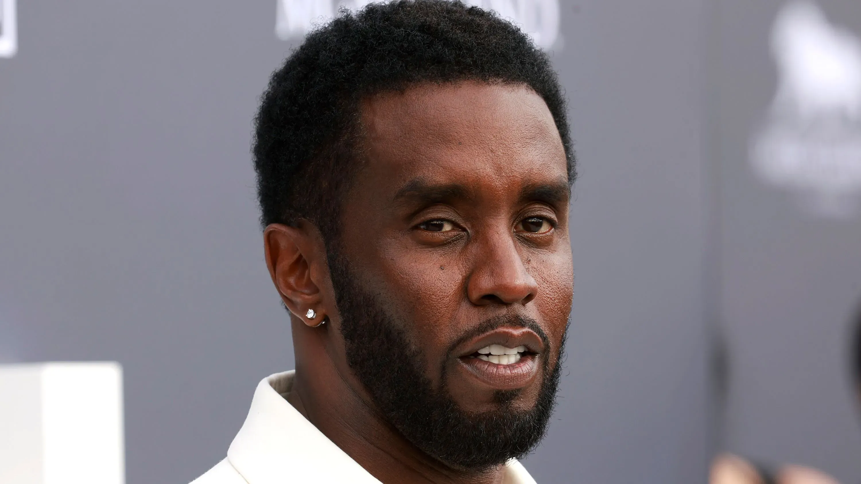 صورة مقربة لرجل ذو لحية قصيرة وشعر مجعد، يبدو وكأنه يتحدث بجدية، مما يعكس التوترات المرتبطة بمحاكمته.