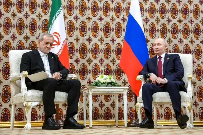 اجتماع بين الرئيس الإيراني إبراهيم رئيسي والرئيس الروسي فلاديمير بوتين، مع العلم الإيراني والروسي في الخلفية، يعكس التعاون بين البلدين.