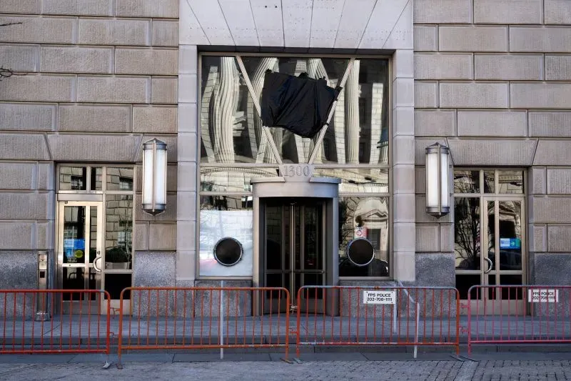 واجهة مبنى حكومي مغلقة، مع وجود حواجز وعلم أسود معلق، تعكس التوترات السياسية والقرارات المثيرة للجدل في الحكومة.