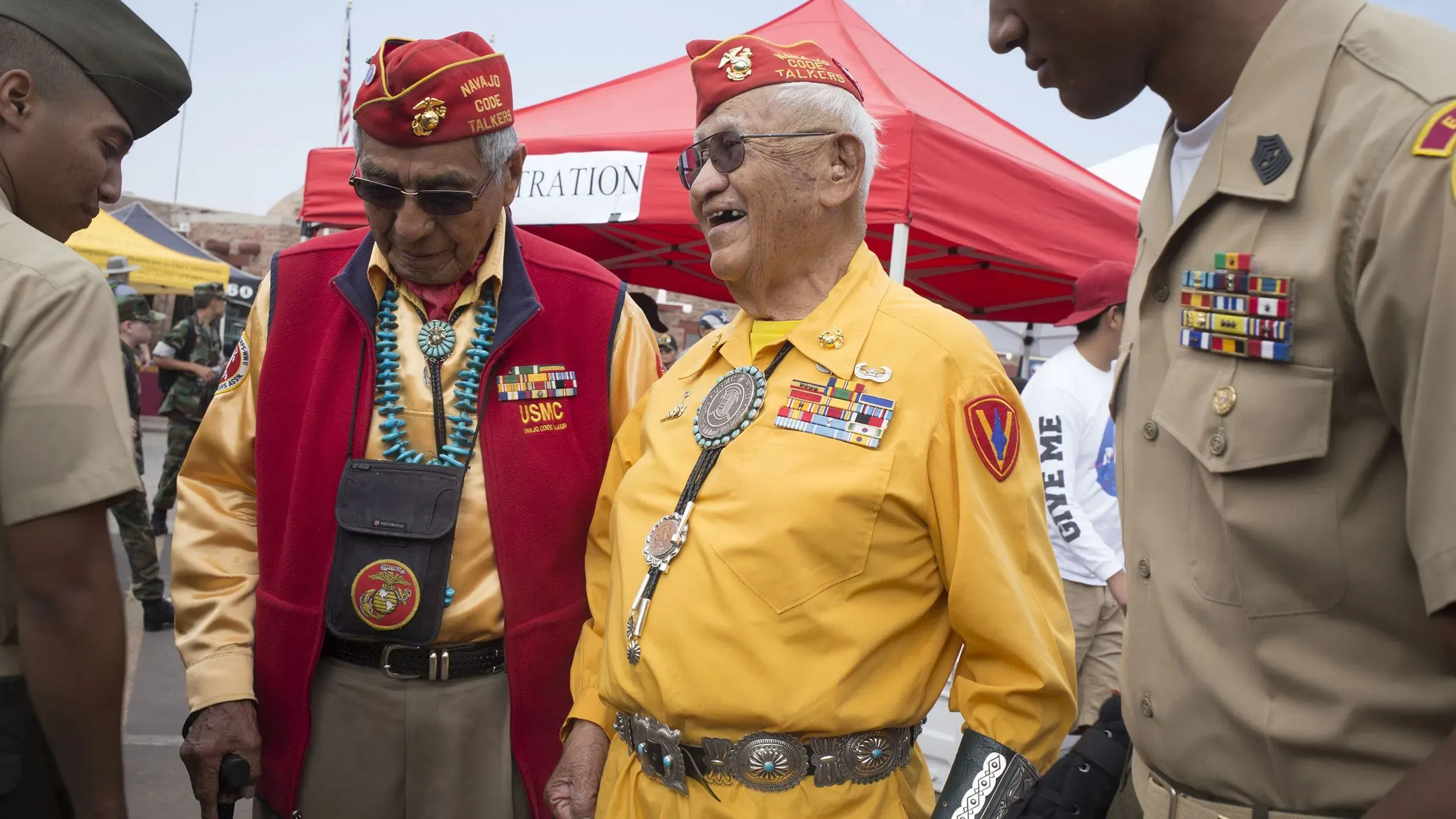 احتفال بمناسبة اليوم الوطني للمتحدثين بشفرة نافاجو، يظهر قدامى المحاربين يرتدون زيهم العسكري، يتبادلون الحديث مع جنود.