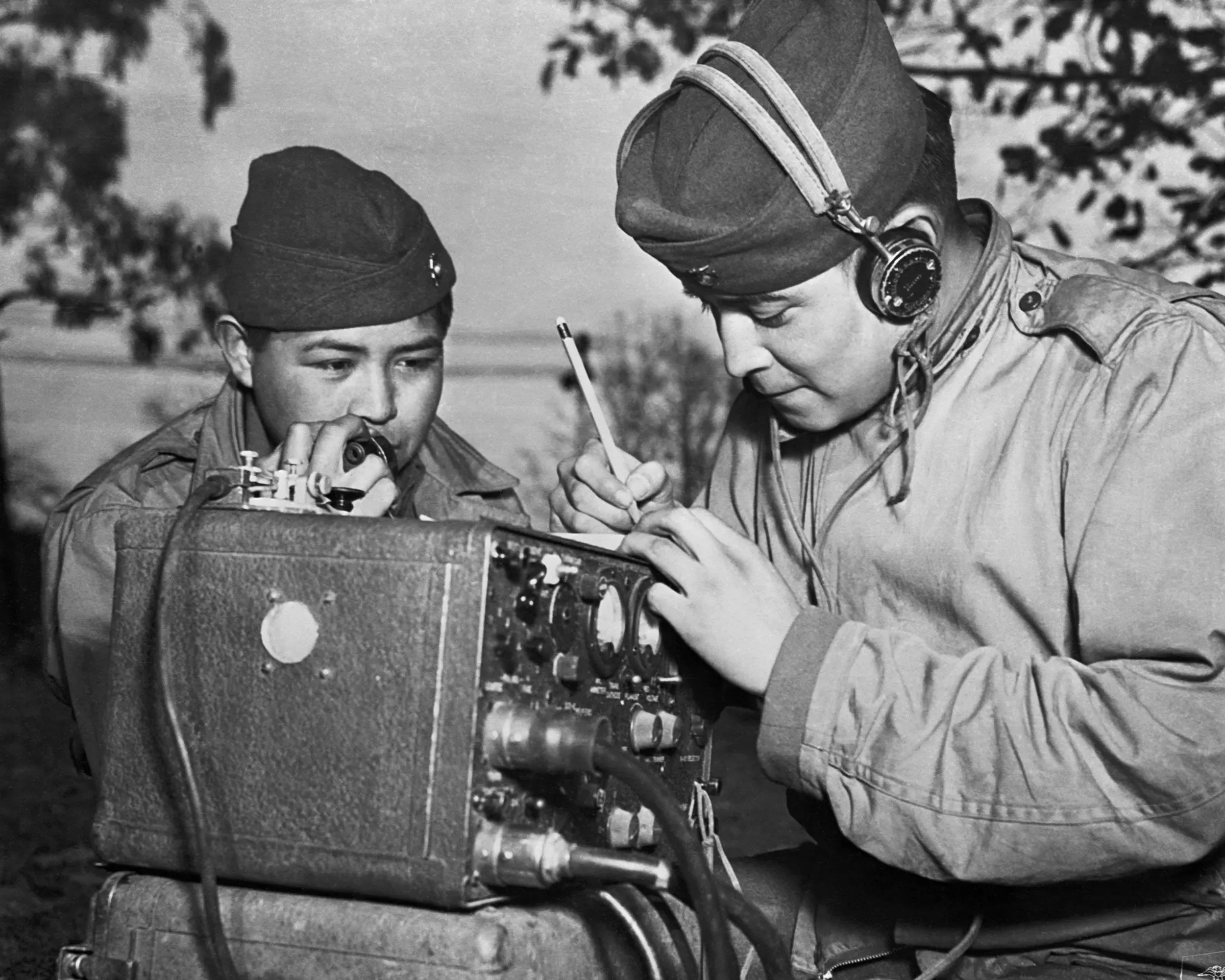 صورة تاريخية لاثنين من متحدثي شفرة نافاجو أثناء استخدامهم جهاز إرسال لاسلكي خلال الحرب العالمية الثانية، مع التركيز على دورهم الحيوي في الاتصالات العسكرية.
