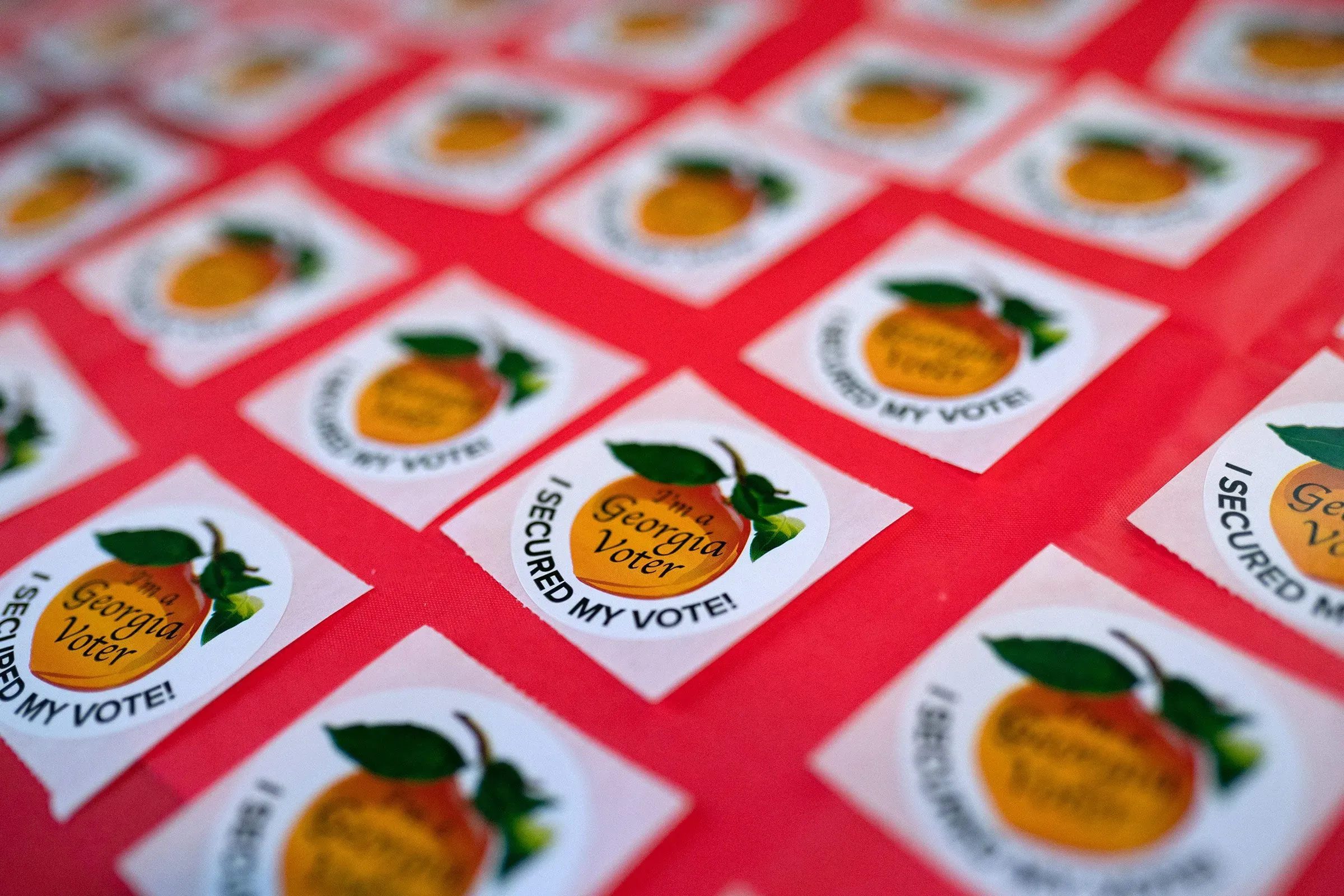 ملصقات تحمل عبارة "أنا ناخب في جورجيا" و"لقد ضمنت صوتي!"، موضوعة على سطح أحمر، تعبر عن أهمية المشاركة الانتخابية.