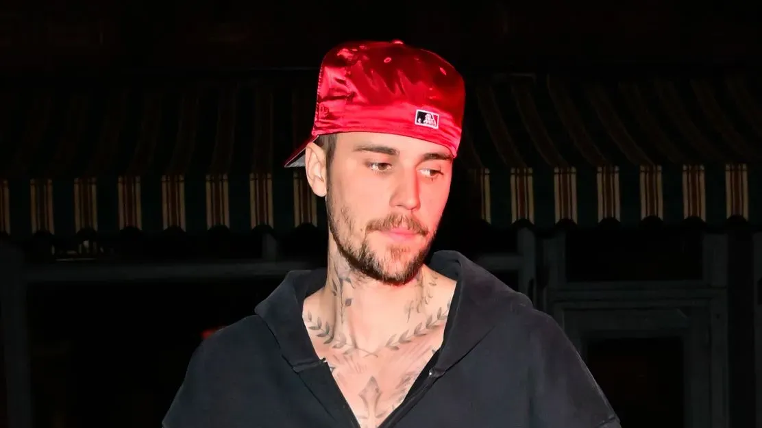 جاستن بيبر يتحدث عن مشاعر عدم الاستحقاق والقلق بشأن صحته، مرتديًا قبعة حمراء في صورة تظهره بتعب واضح.