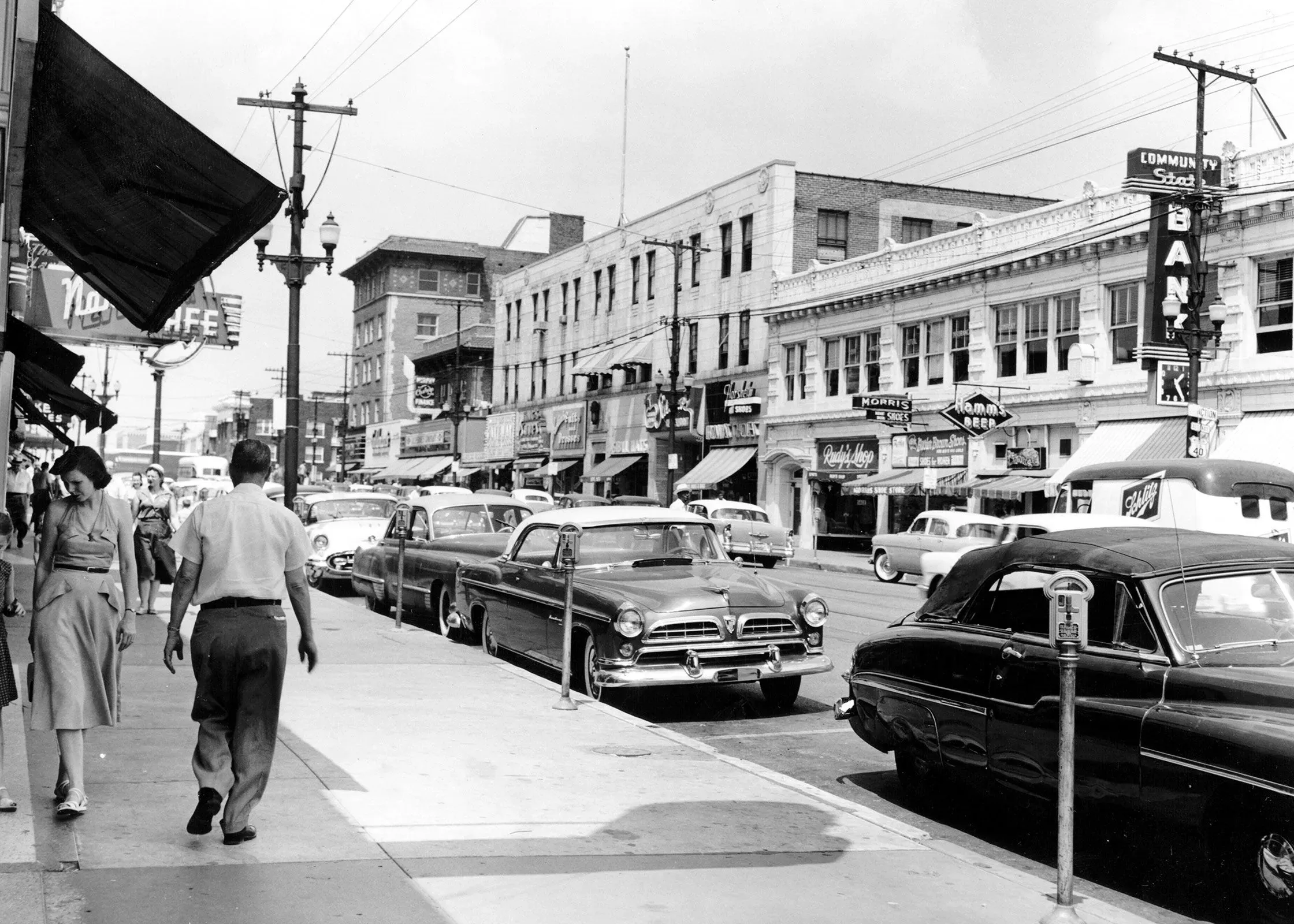 شارع تروست في مدينة كانساس سيتي، يظهر فيه مشاة وسيارات من خمسينيات القرن الماضي، مع واجهات متاجر قديمة تعكس تاريخ الفصل العنصري.