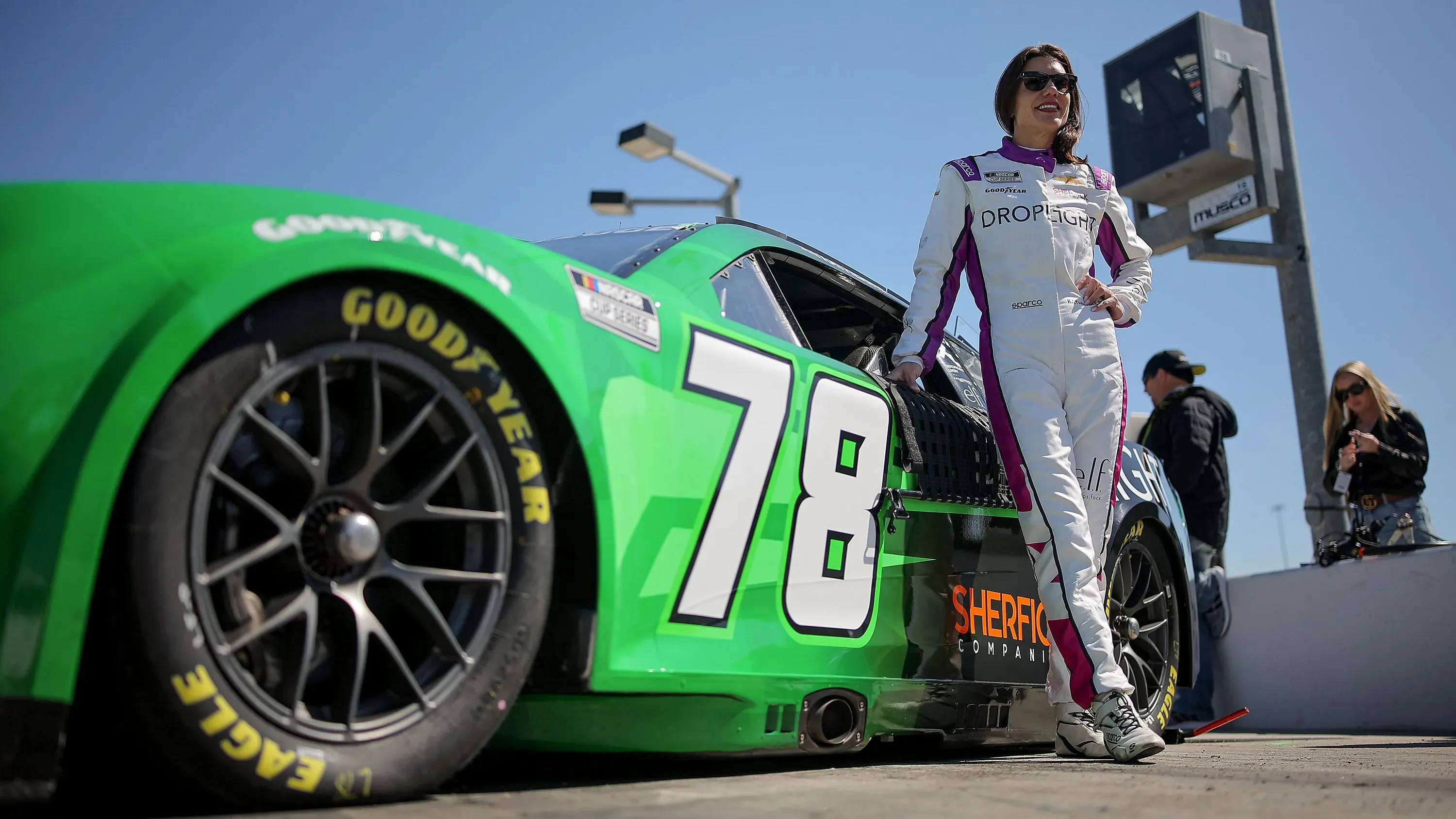 كاثرين ليج، سائقة سباقات بريطانية، تقف بجانب سيارتها الخضراء رقم 78 في حلبة فينيكس، تعكس لحظة تاريخية في رياضة السيارات.