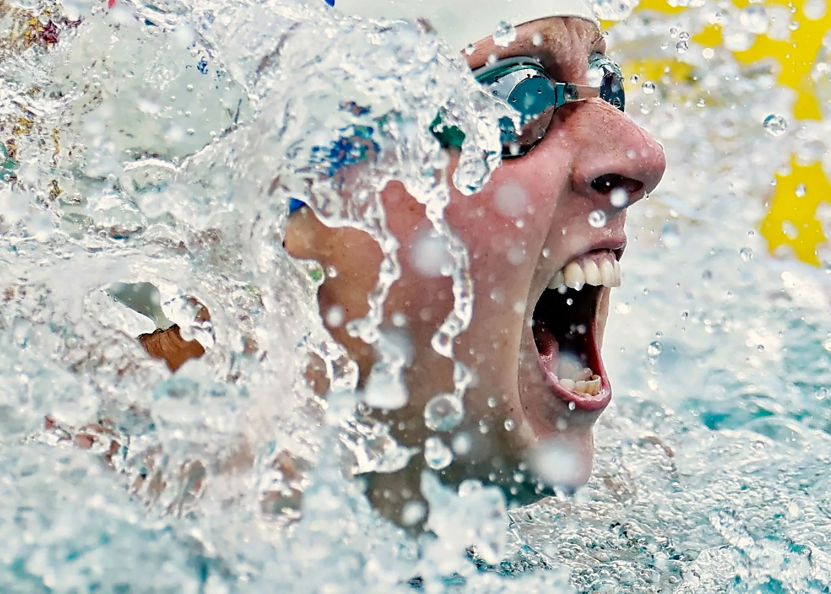 سباح يصرخ في حماس أثناء التدريب، محاطاً برذاذ الماء، مع التركيز على الأداء القوي والاستعداد لبطولة العالم في السباحة.