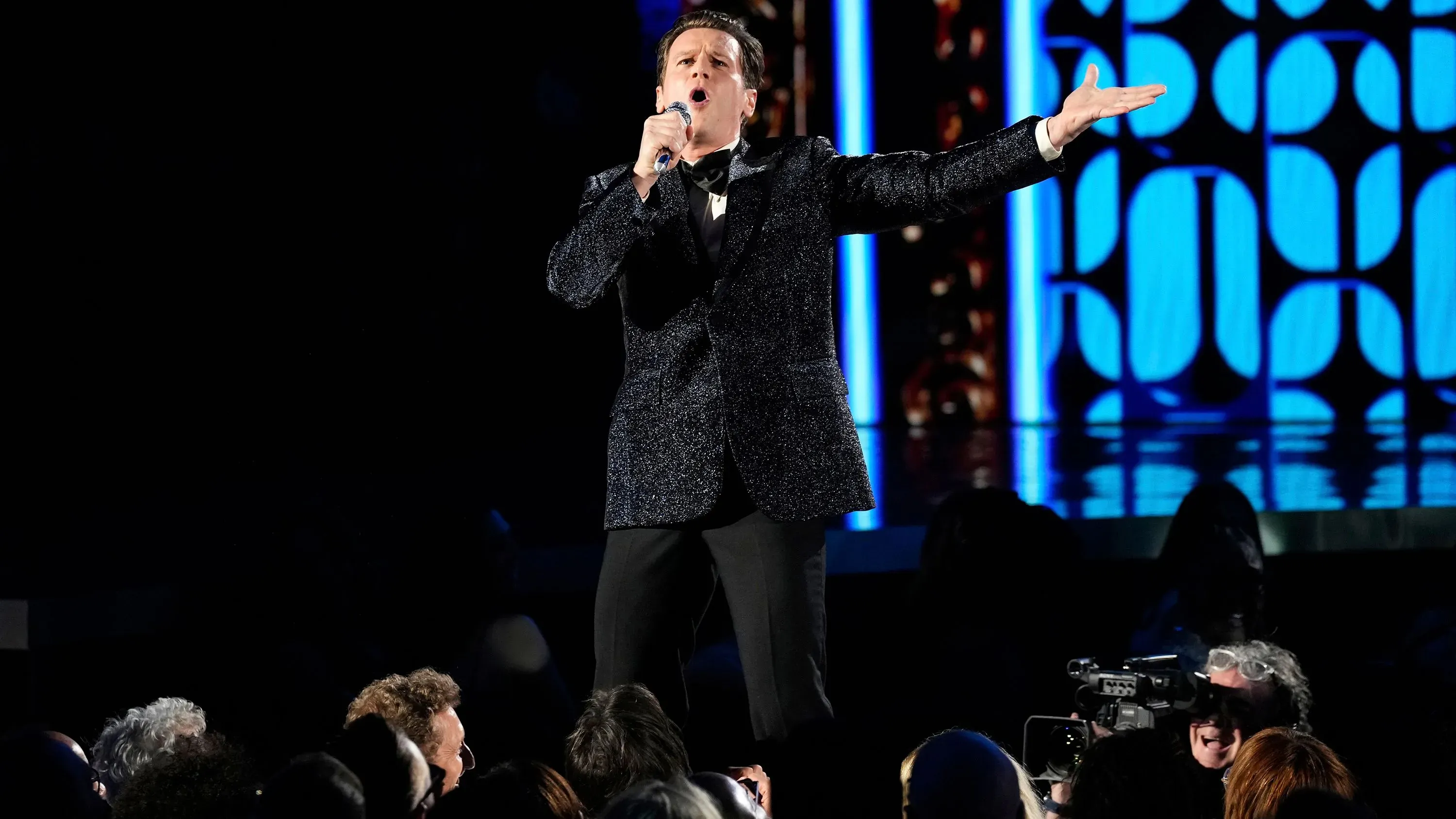 جوناثان جروف يؤدي أغنية "ماك ذا نايف" في حفل توزيع جوائز توني، مرتديًا بدلة سهرة لامعة، بينما يتفاعل الجمهور معه.