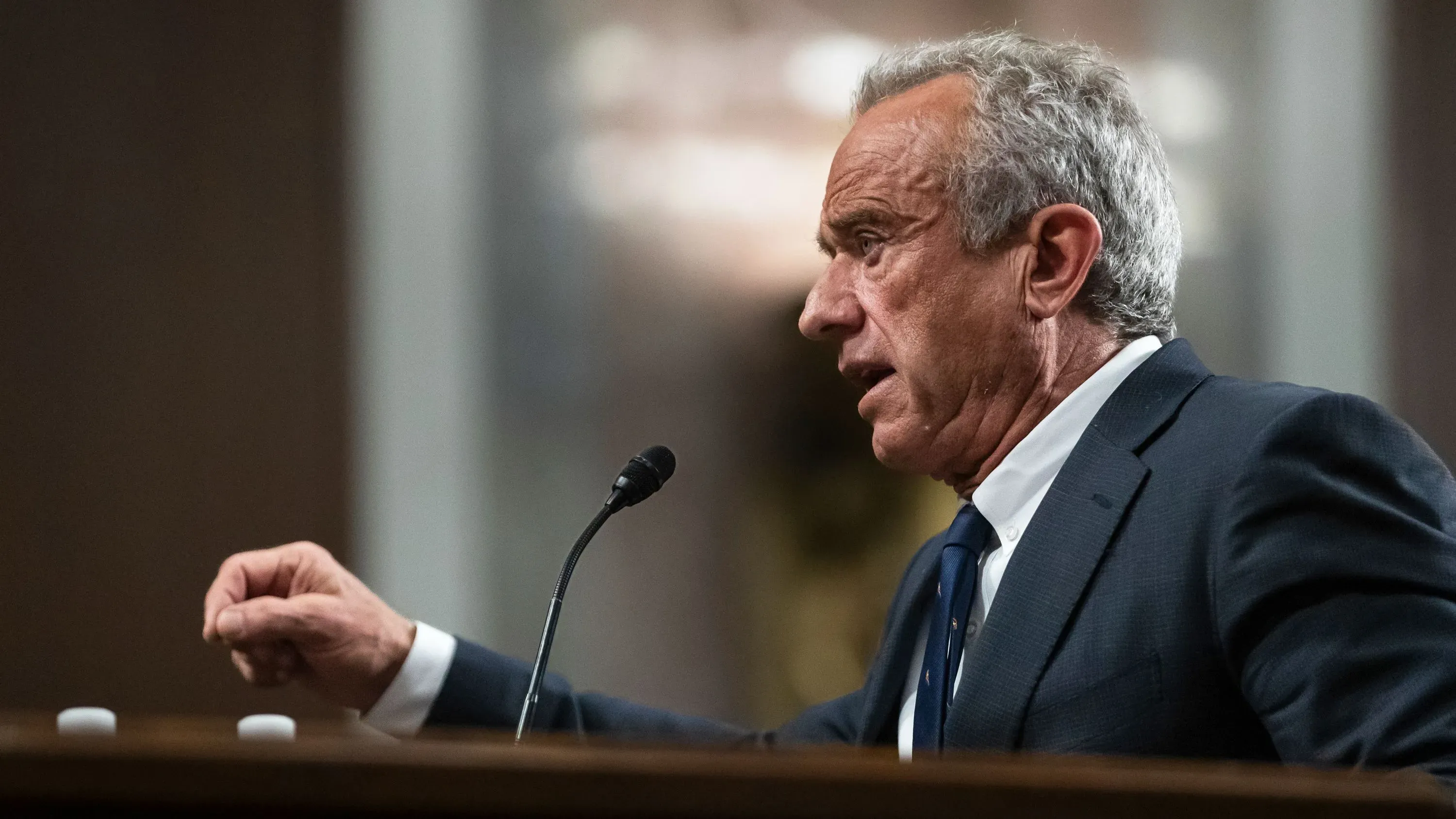 شخص يتحدث في جلسة استماع، مع التركيز على تعبيرات وجهه وحركات يده، في سياق مناقشة حول تفشي مرض الحصبة والعلاجات المقترحة.