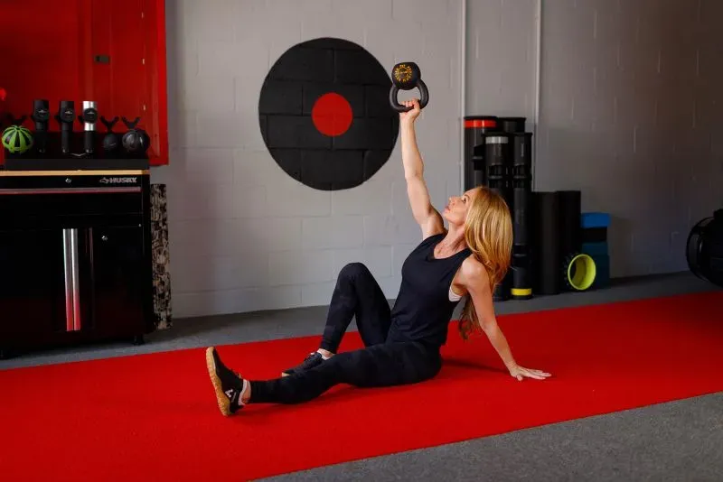 امرأة تؤدي تمرين رفع كتل حديدية على الأرض، وتركز على تقوية العضلات لتحسين الحركة والحفاظ على النشاط البدني.