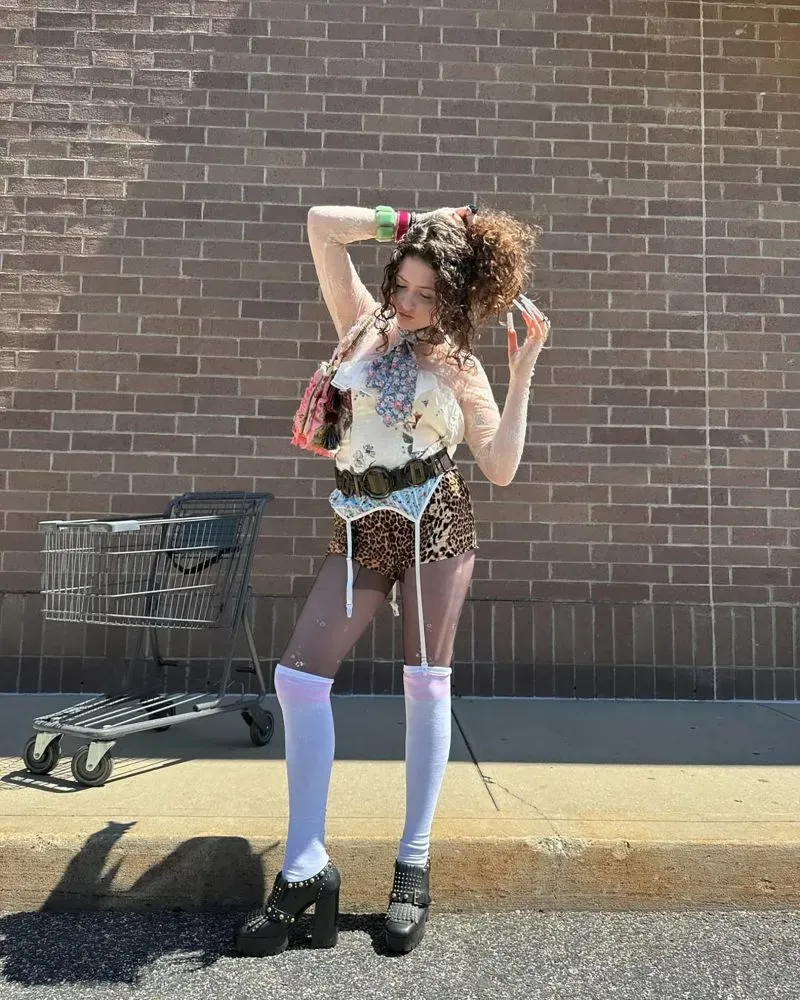 امرأة ترتدي ملابس جريئة ومتنوعة، تشمل قميصًا شفافًا وسروالًا مزخرفًا بنمط النمر، وتستعرض أسلوبها الفريد في الأزياء.