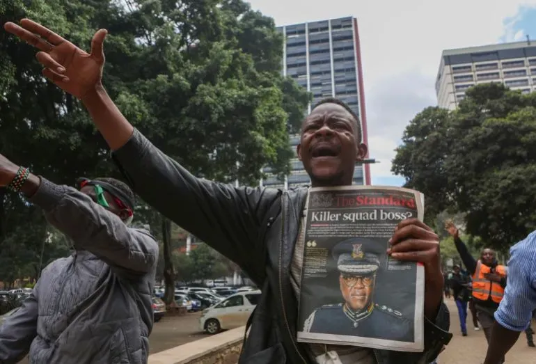 رجل يحتج في نيروبي، يحمل صحيفة تتحدث عن قائد وحدة القتل، مع تعبيرات وجه تعكس الغضب والمطالبة بالعدالة.