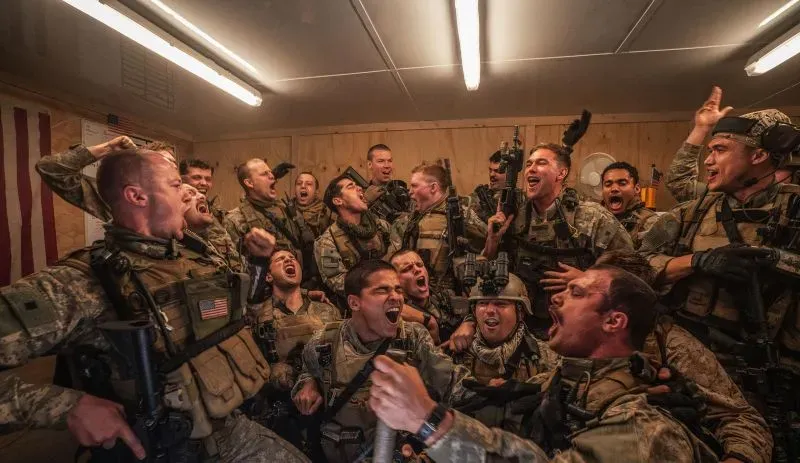 مجموعة من الجنود في غرفة مغلقة، يحتفلون ويعبرون عن حماسهم، مرتدين زيهم العسكري، في أجواء من الفرح والتضامن.