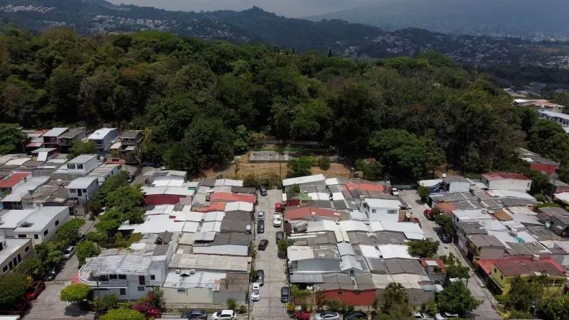 صورة جوية لحي سكني في السلفادور، تظهر منازل متراصة تحت أشجار كثيفة، تعكس الظروف المعيشية والتحديات التي واجهها أبريغو غارسيا.