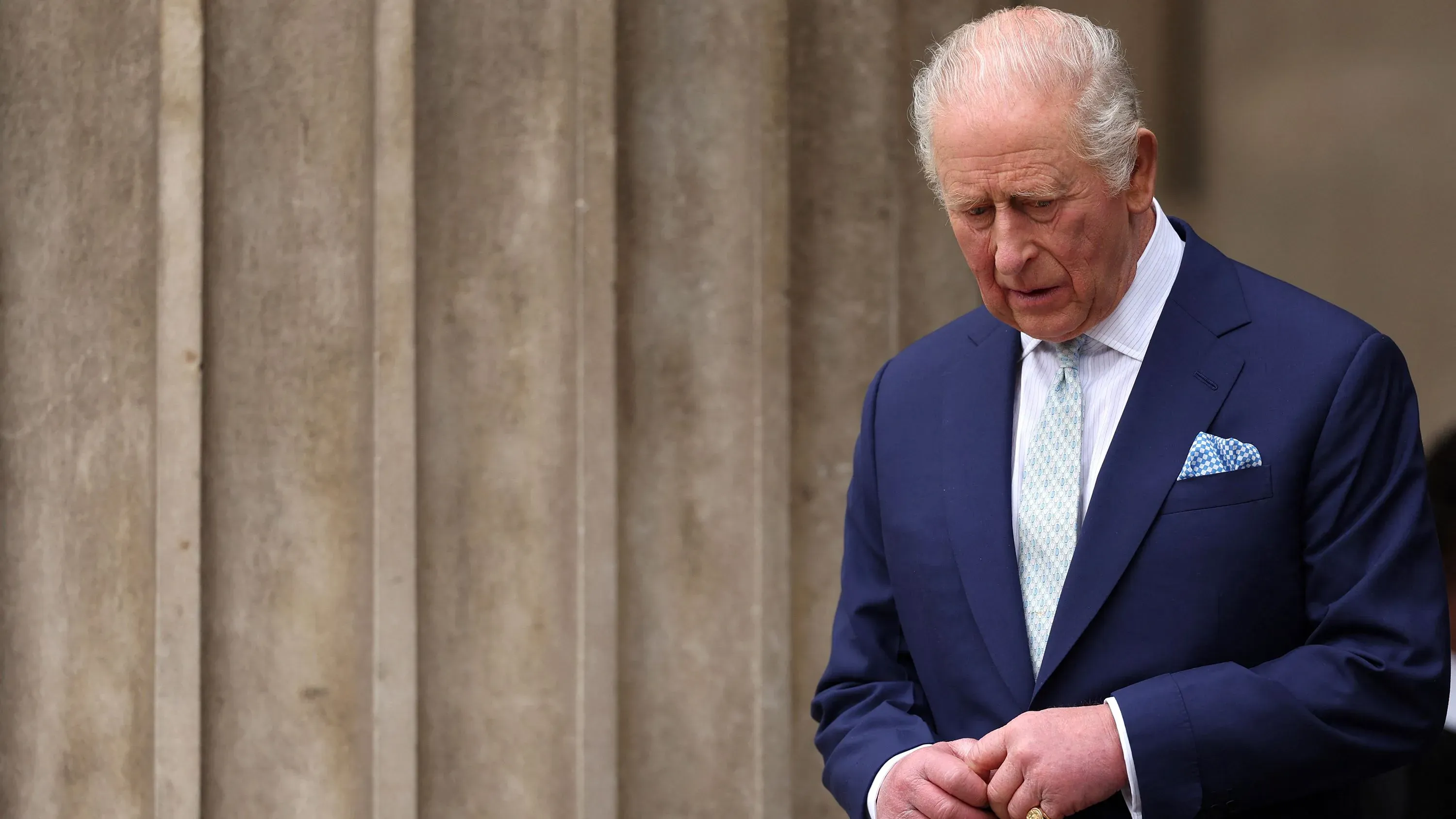 الملك تشارلز الثالث يرتدي بدلة زرقاء، متأملاً بجدية أثناء حدث رسمي، مما يعكس التوترات الحالية في العلاقات البريطانية الأمريكية.