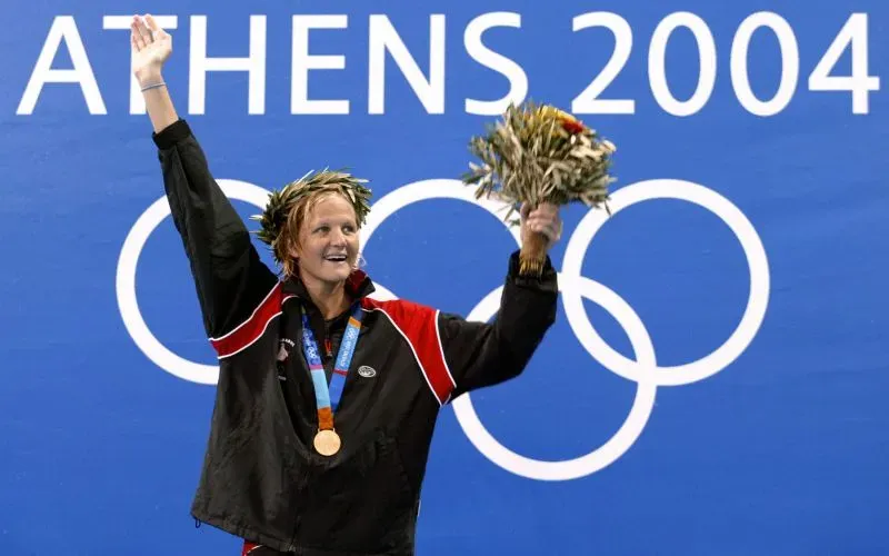 كيرستي كوفنتري تحتفل بفوزها بالميدالية الذهبية في أولمبياد أثينا 2004، مرتديةً زيها الرياضي وتحمل غصن زيتون.