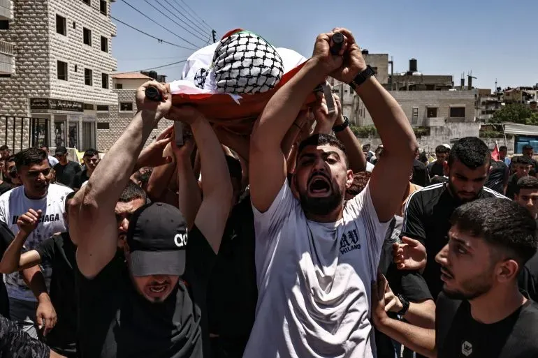 محتجون يحملون جثمان فلسطيني مغطى بعلم فلسطين خلال جنازته، وسط أجواء من الحزن والغضب في الضفة الغربية.