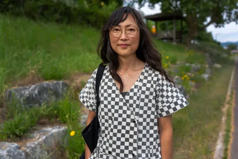 امرأة ترتدي فستانًا مخططًا باللونين الأسود والأبيض، تقف في منطقة خضراء، تعكس قصة البحث عن الهوية والعائلة.