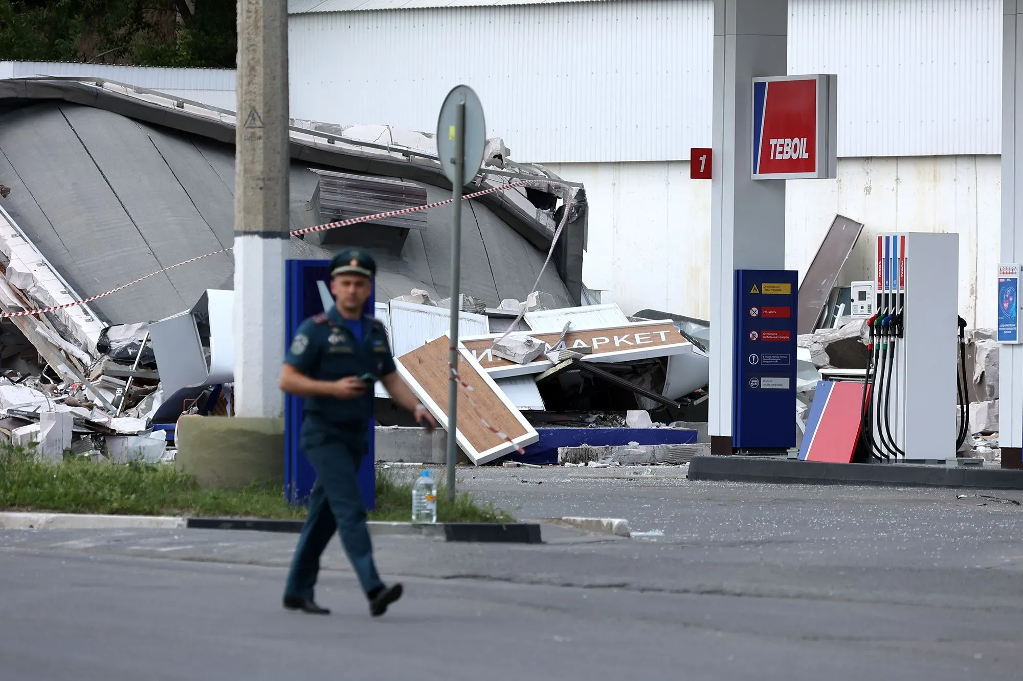 تظهر الصورة رجلًا يرتدي زيًا رسميًا يسير بالقرب من محطة وقود مدمرة، مما يعكس تأثير نقص الوقود في القرم بسبب الصراعات.