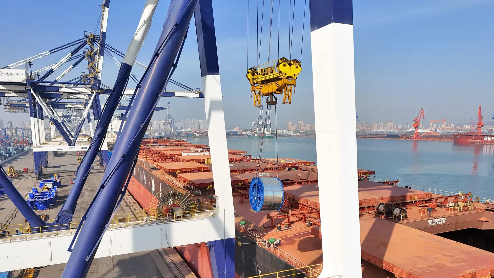 صورة لميناء بحري حيث تُرفع حاوية كبيرة بواسطة رافعة، مع سفن شحن في الخلفية. تعكس الصورة تأثير التعريفات الجمركية على التجارة.