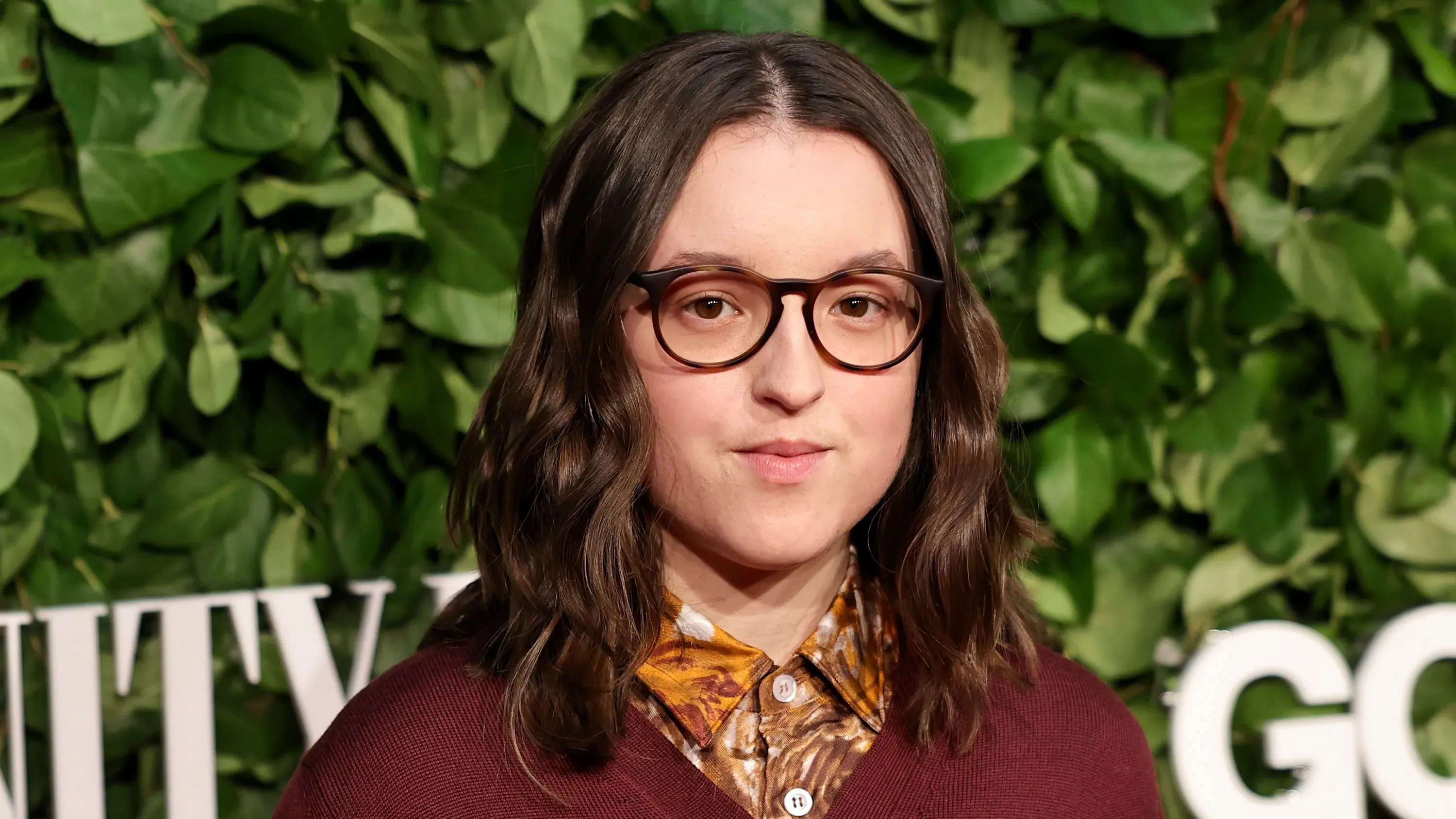 بيلا رامزي، نجمة "The Last of Us"، تتحدث عن تجربتها مع التوحد وتأثيره على تمثيلها، مع خلفية نباتية خضراء.