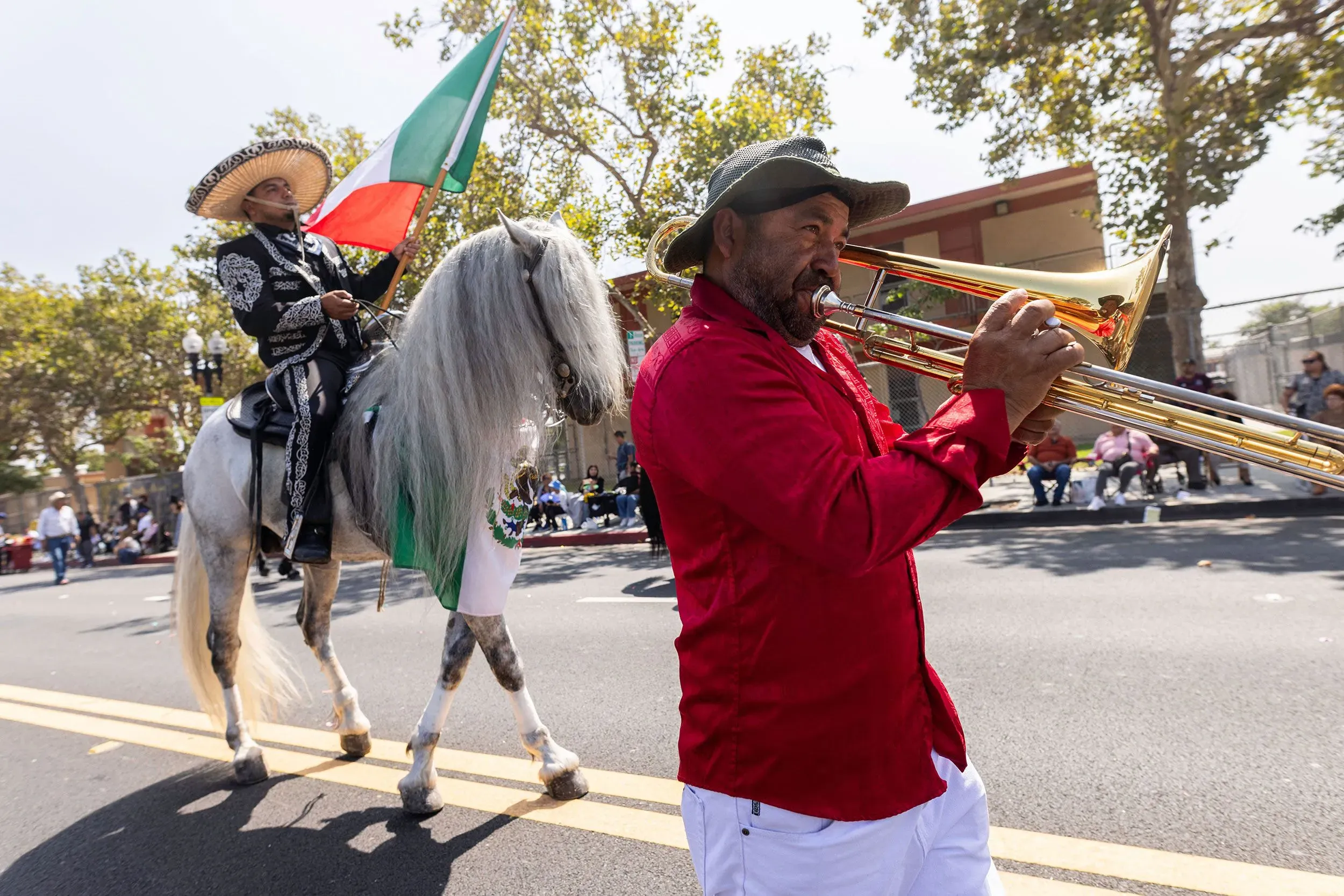 رجل يعزف على الترومبون بينما يركب آخر حصانًا أبيض ويرفع علم المكسيك، خلال احتفالات يوم الاستقلال في كاليفورنيا.