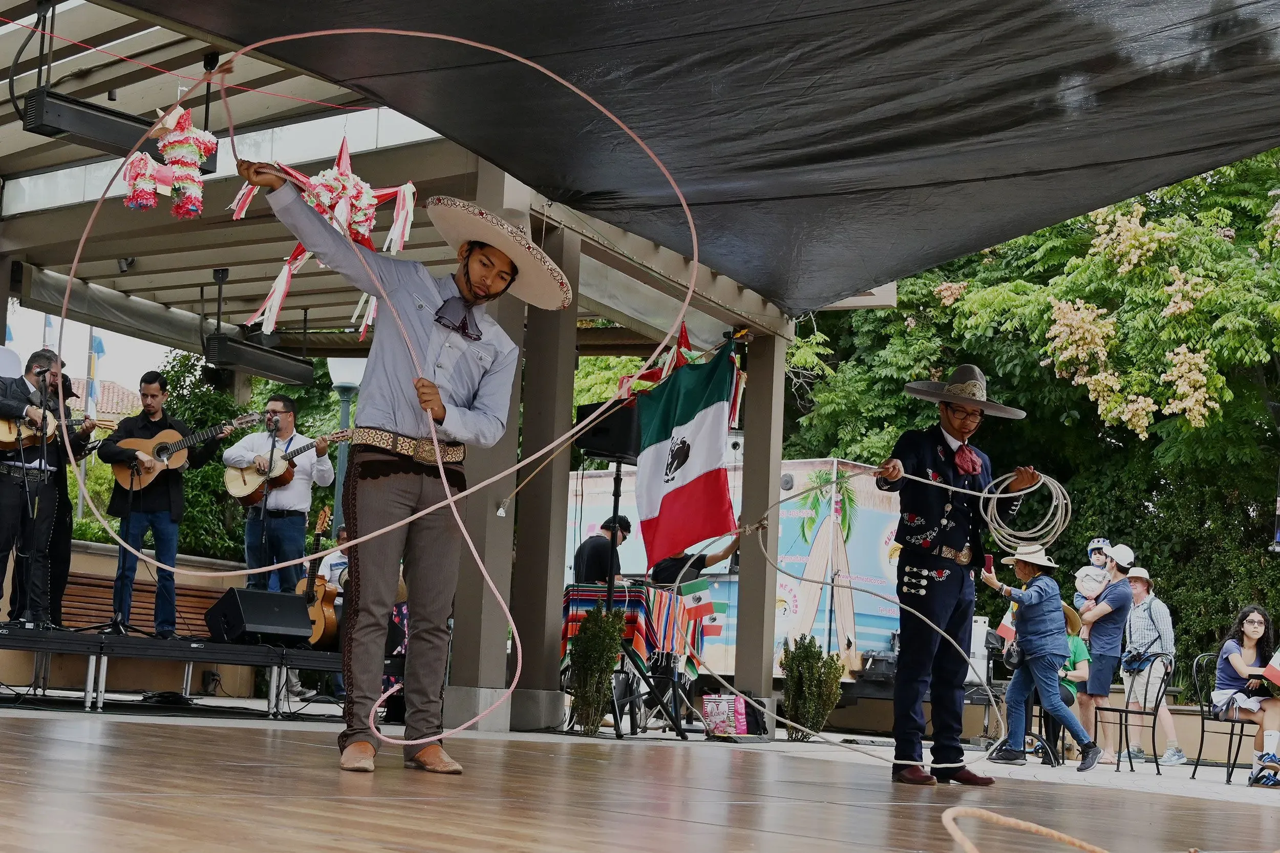 شبان يرتديان ملابس تقليدية مكسيكية يؤدون عرضًا فنيًا باستخدام الحبال في احتفال بيوم استقلال المكسيك، مع وجود جمهور خلفهم.