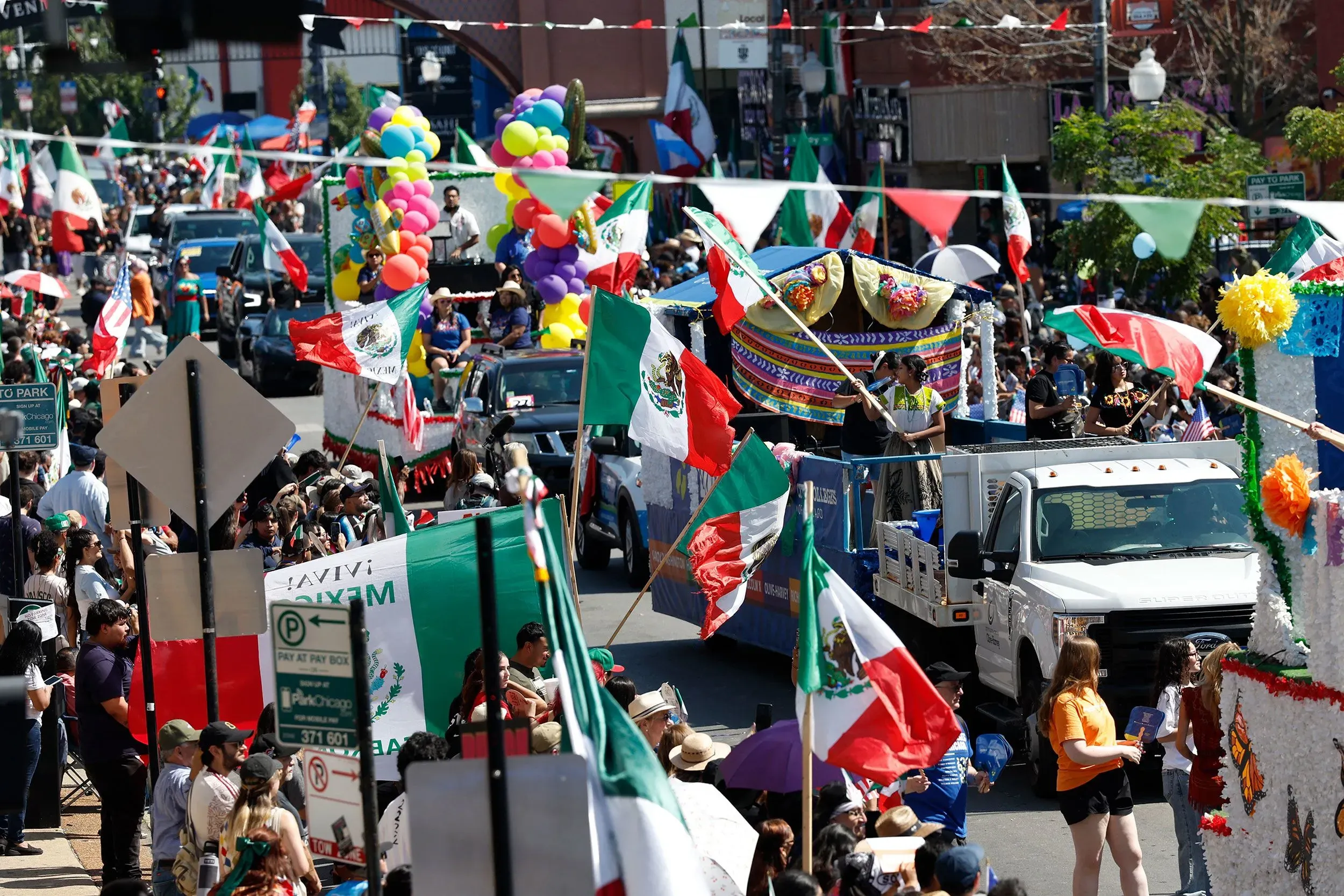 احتفال بمناسبة يوم استقلال المكسيك في شوارع ملونة، حيث يرفع المشاركون الأعلام المكسيكية، مع وجود سيارات مزينة وحشود من الناس.