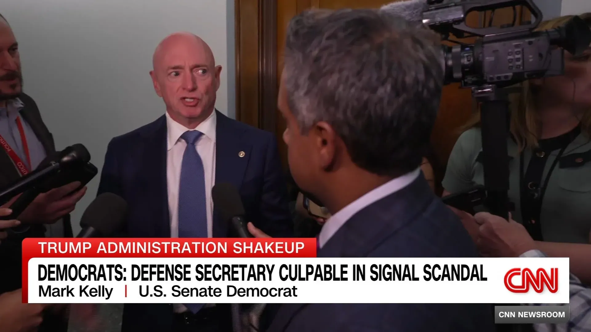 لقاء صحفي لمارك كيلي، عضو مجلس الشيوخ الأمريكي، يتحدث عن إقالة مستشار الأمن القومي في إدارة ترامب، مع وجود صحفيين ومصورين حوله.