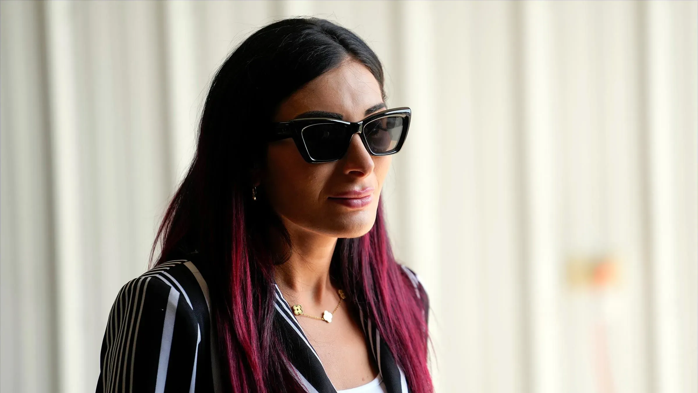 لورا لومر ترتدي نظارات شمسية وتظهر تعبيرًا جادًا، في سياق مناقشة تأثيرها على إدارة ترامب وتحدياتها للحصول على أوراق اعتماد صحفية.