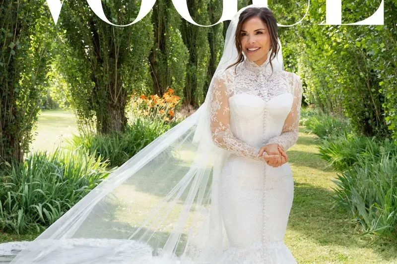 فستان زفاف لورين سانشيز من دولتشي آند غابانا، بتصميم أنيق ذو رقبة عالية وطرحة تقليدية، محاط بطبيعة خضراء.