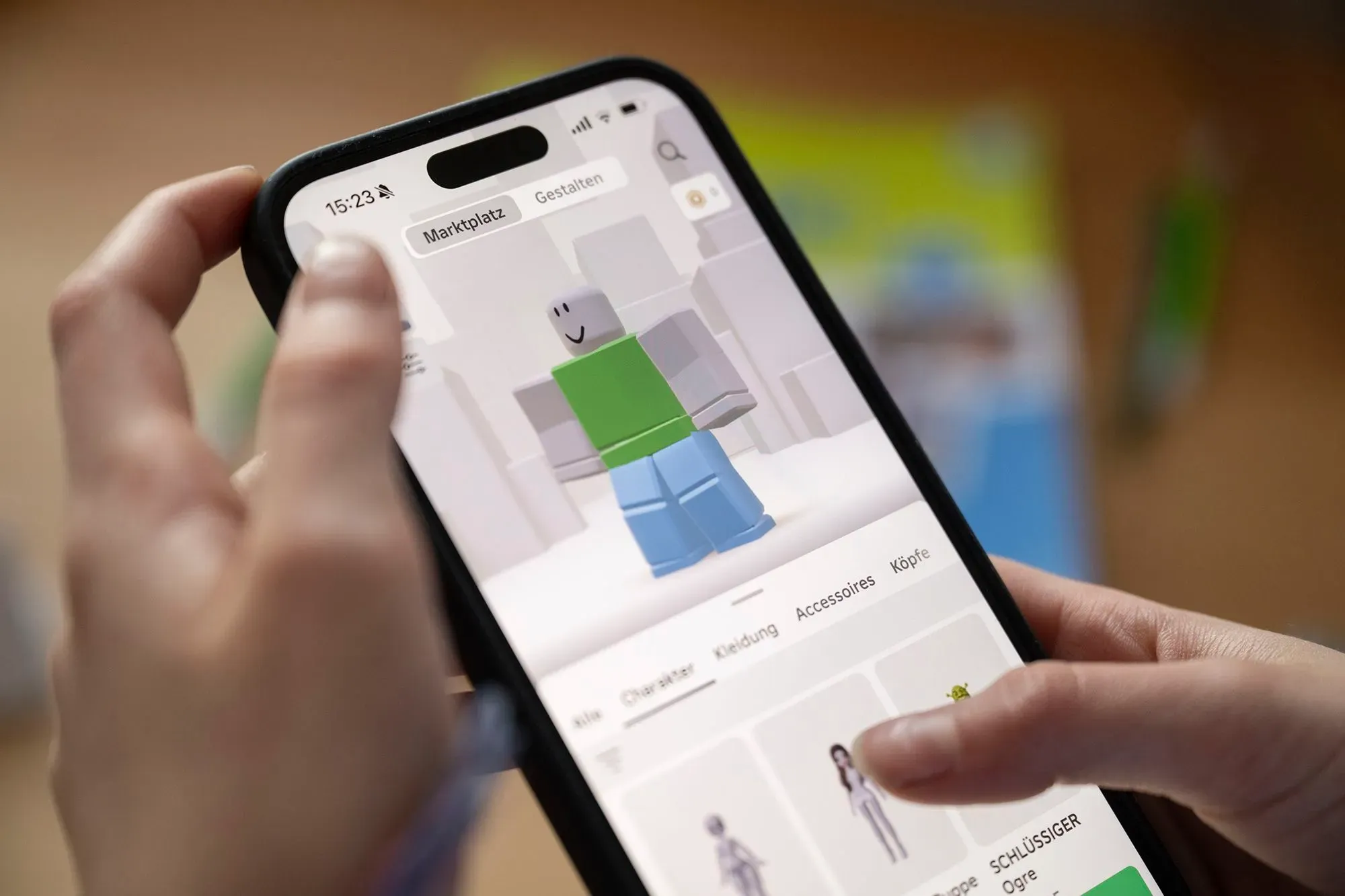واجهة تطبيق Roblox تعرض شخصية افتراضية مع خيارات تخصيص، بينما يستخدم المستخدم الهاتف الذكي للتفاعل مع المنصة.