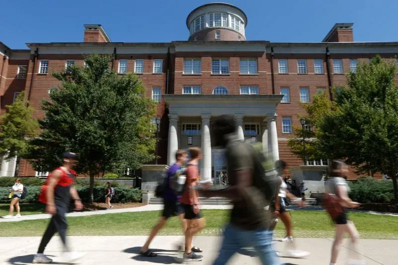 طلاب أجانب يتجولون في حرم جامعي، مع مبنى أكاديمي كبير في الخلفية، وسط قضايا قانونية تتعلق بوضعهم القانوني في الولايات المتحدة.