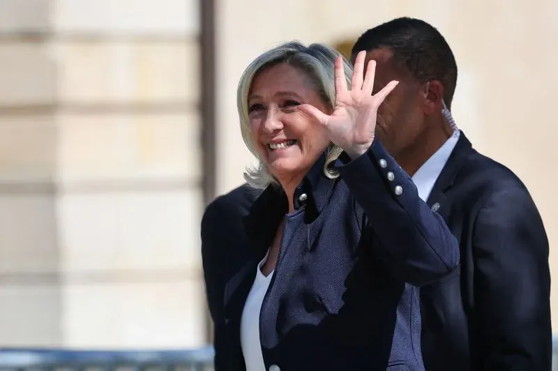 مارين لوبان، زعيمة حزب التجمع الوطني الفرنسي، تبتسم وتلوح بيدها، وسط حشد من أنصارها في باريس، تعبيرًا عن دعمهم لها بعد الحكم القضائي.