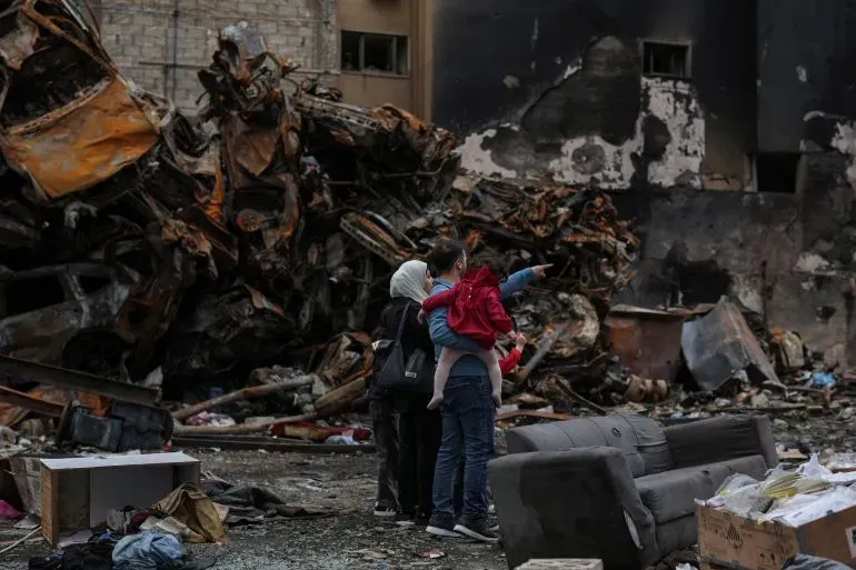 عائلة تتفقد الأضرار في منطقة مدمرة، حيث تظهر السيارات المحترقة والخراب، في سياق التوترات المستمرة بين لبنان وإسرائيل.