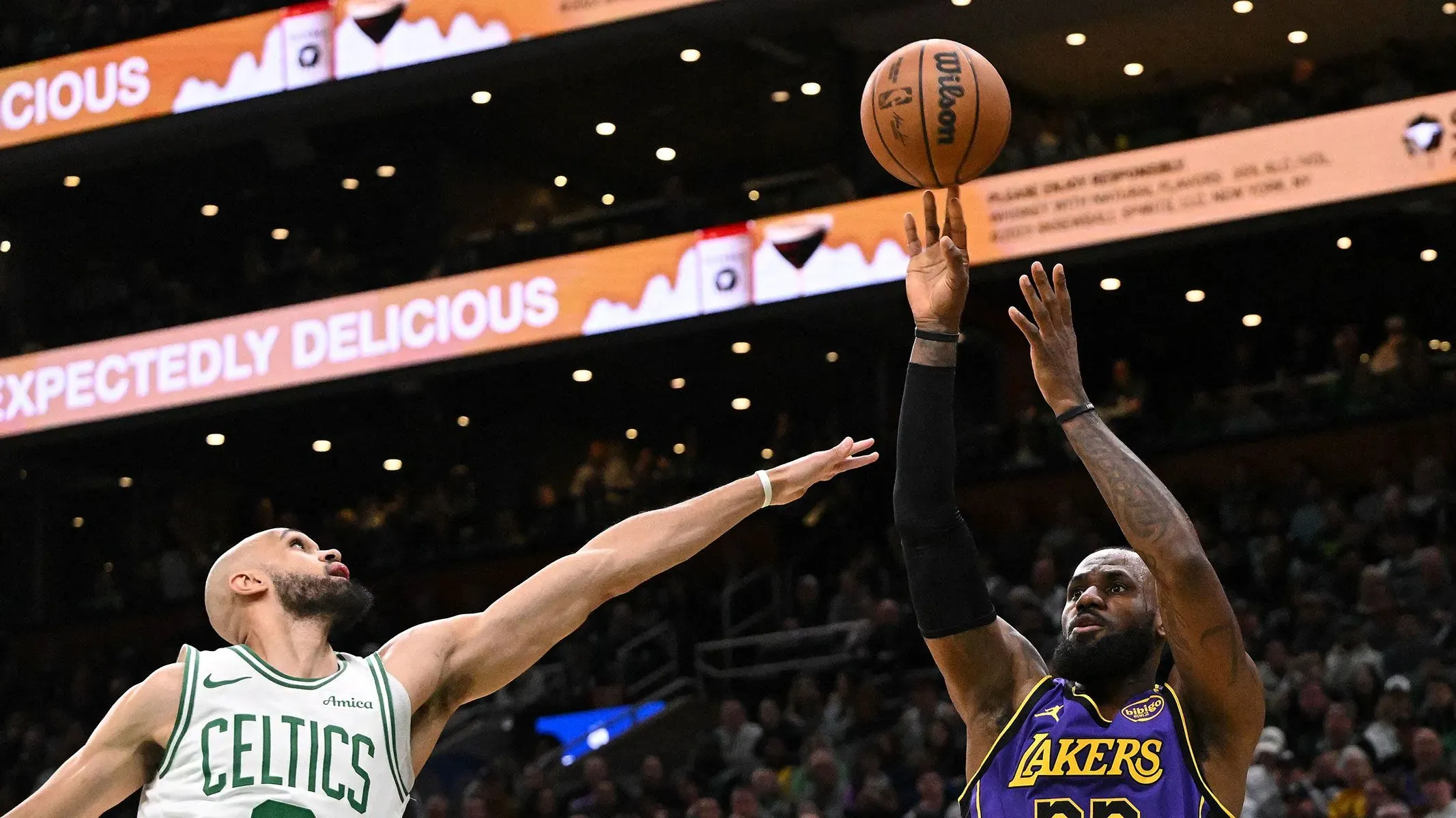 ليبرون جيمس يسجل نقطة في مباراة كرة سلة، بينما يحاول لاعب من فريق سلتكس الدفاع عنه. تُظهر الصورة الأجواء الحماسية للعبة.