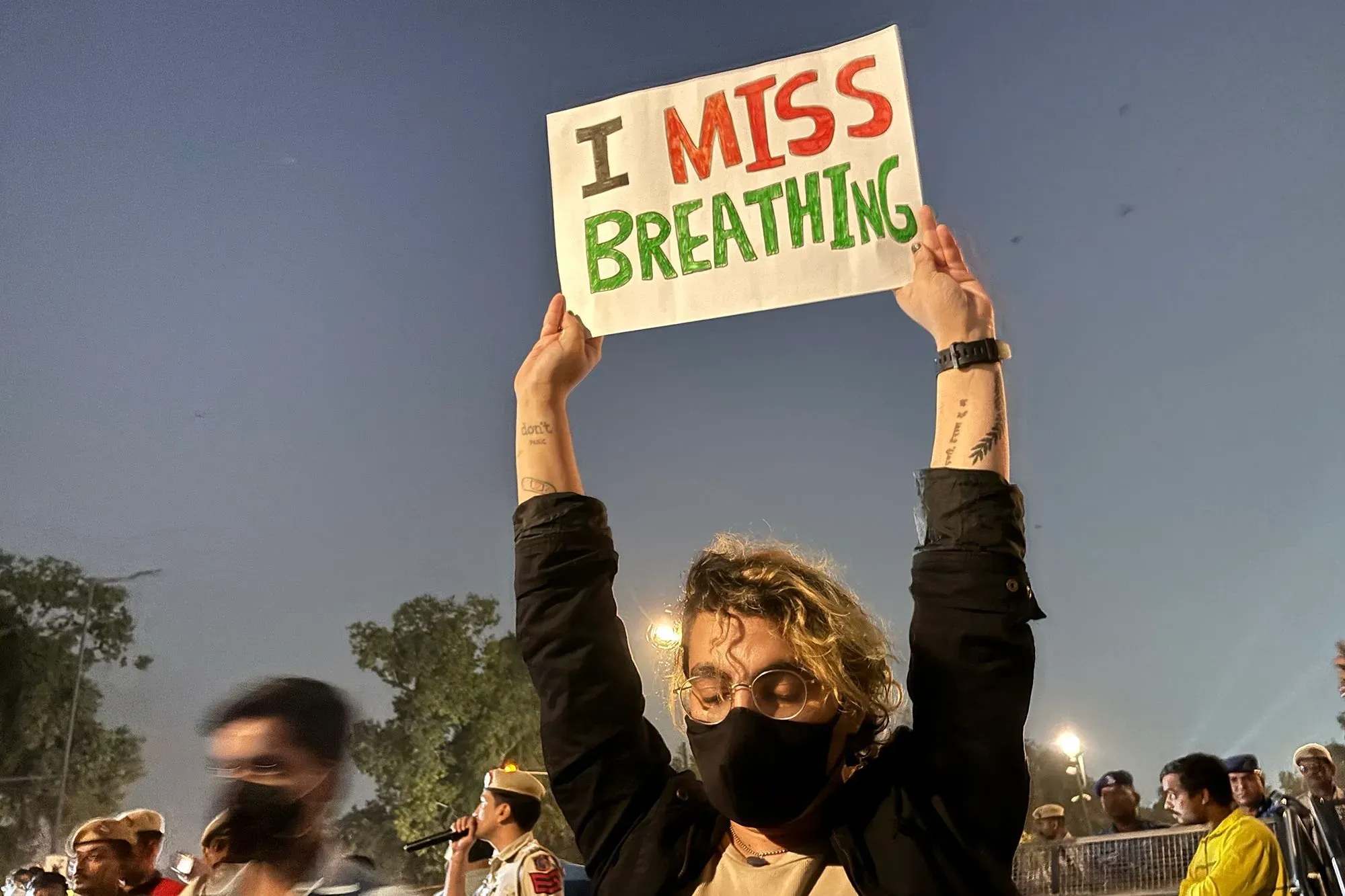 محتج في نيودلهي يحمل لافتة مكتوب عليها "أفتقد التنفس"، مع وجود حشود خلفه، في سياق أزمة تلوث الهواء.