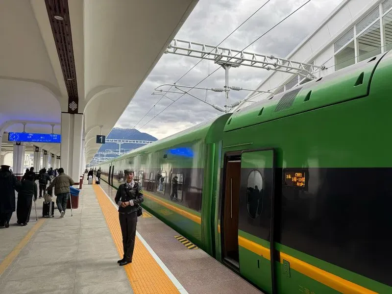 محطة قطار حديثة في التبت، يظهر فيها قطار أخضر اللون، مع وجود مسافرين وضباط أمن، مما يعكس التطورات في البنية التحتية.