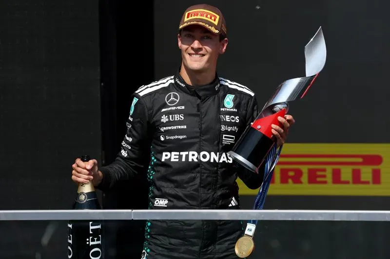 جورج راسل، سائق مرسيدس، مبتسم وهو يحمل الكأس بعد فوزه الأول في سباق جائزة كندا الكبرى، مع زجاجة شمبانيا في اليد.