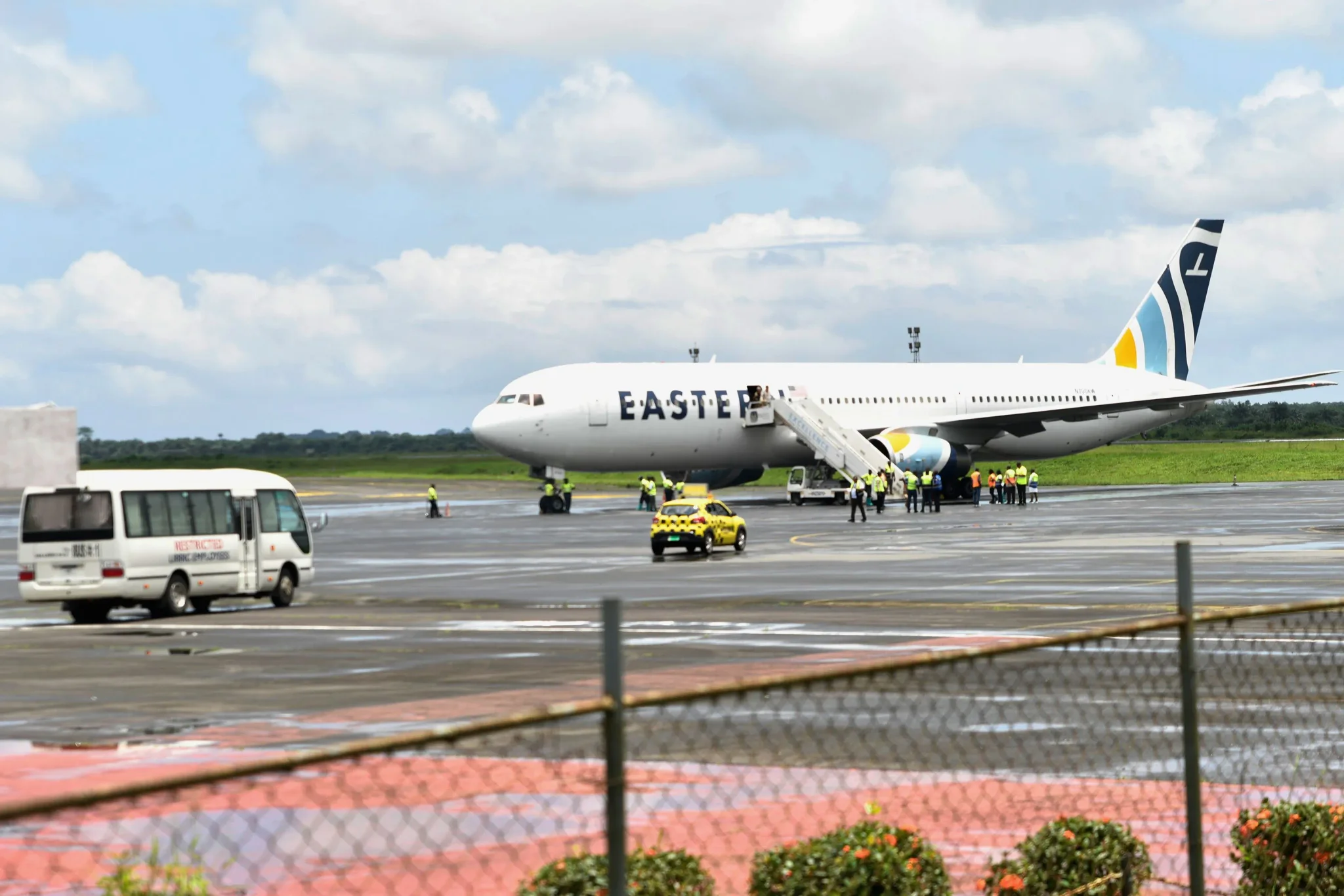 طائرة شركة Eastern Airlines متوقفة في مطار مونروفيا مع وجود أفراد أمن وحافلة، تعكس وصول المهاجرين المرحلين من الولايات المتحدة إلى ليبيريا.