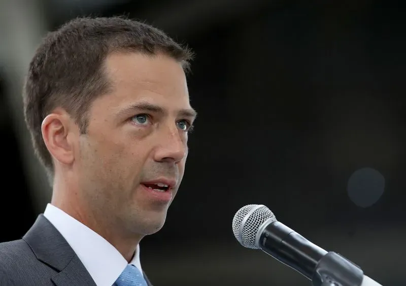 يتحدث رجل في بدلة رسمية أمام ميكروفون، معبرًا عن المخاوف المتعلقة بتقليص عدد موظفي الأرصاد الجوية وتأثيره على التنبؤات الجوية.