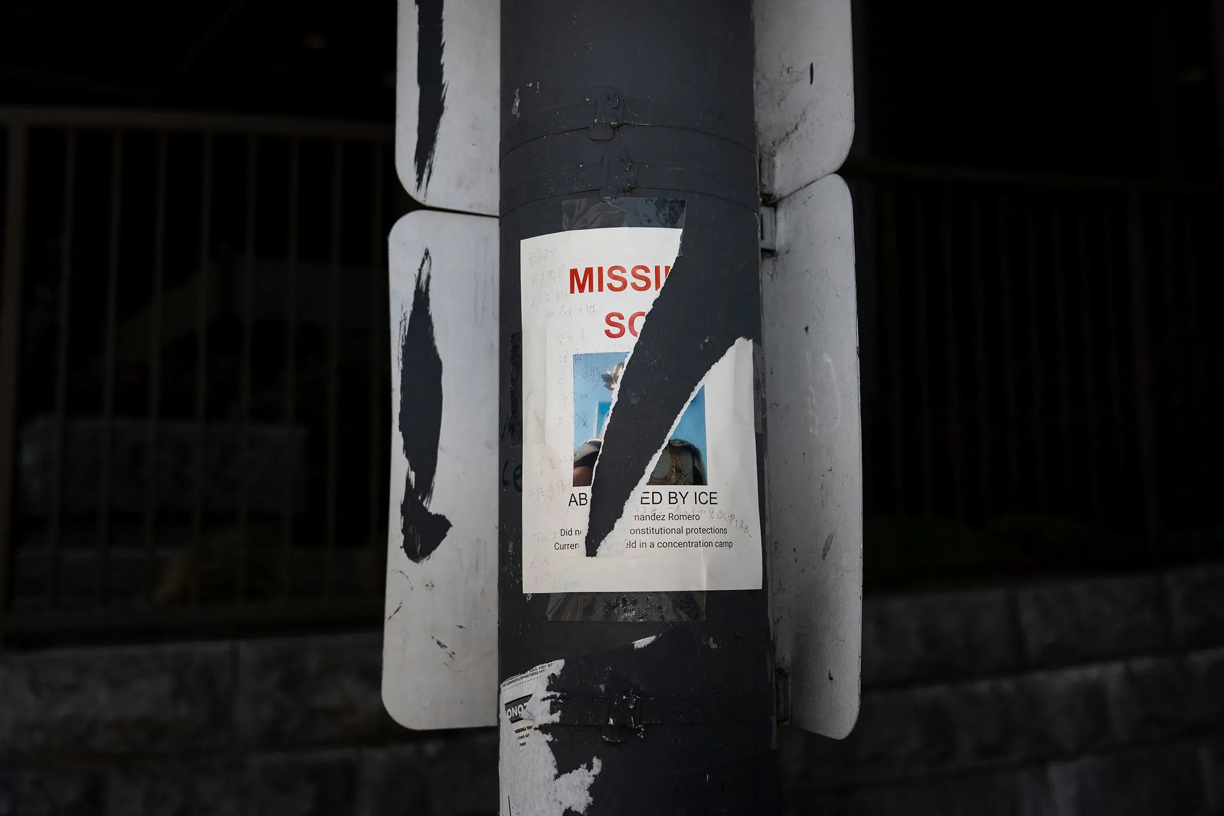 ملصق مفقود على عمود، يحمل صورة شخص مفقود يُعتقد أنه تم احتجازه من قبل إدارة الهجرة والجمارك، مع تفاصيل الاتصال.