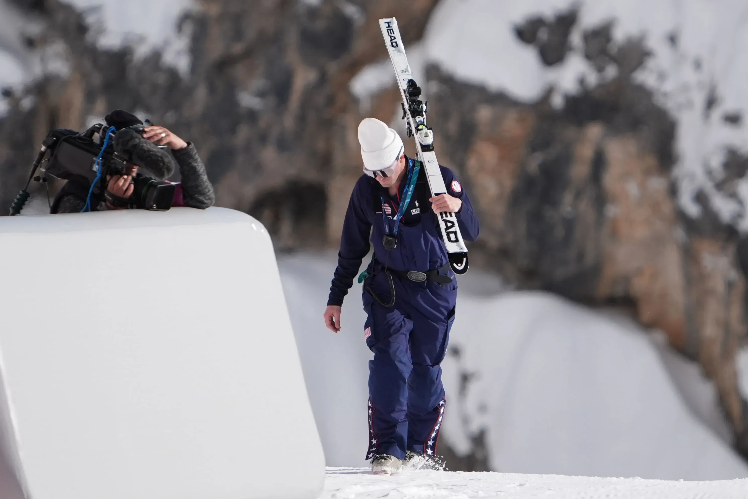 لاعبة التزلج ليندسي فون تحمل زلاجاتها أثناء توجهها نحو نقطة الانطلاق في جبال الدولوميت، مع وجود مصور يلتقط اللحظة.