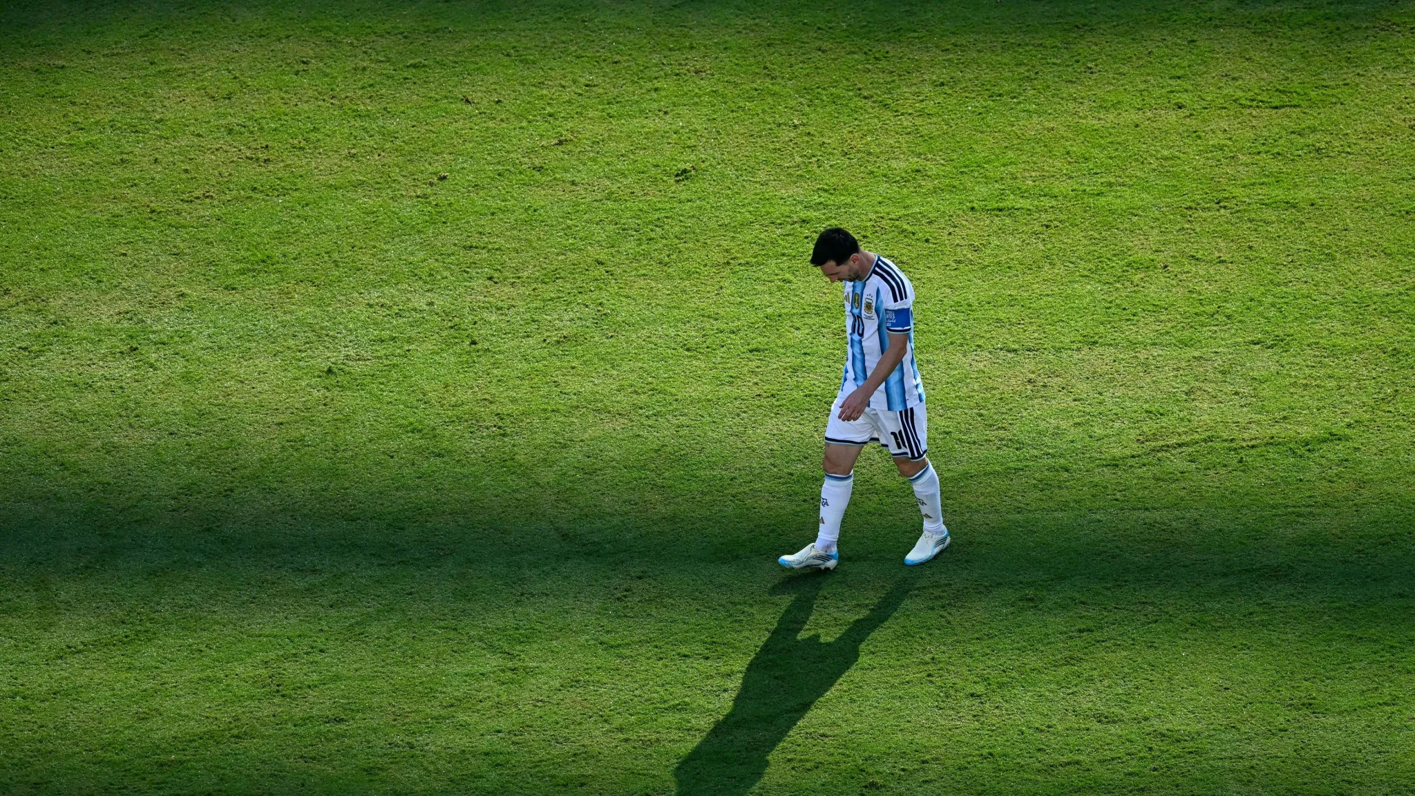 ليونيل ميسي يسير وحيداً على أرض الملعب بظل طويل، معبرًا عن لحظة تأمل وحزن بعد خسارة المنتخب الأرجنتيني في مباراة مهمة.