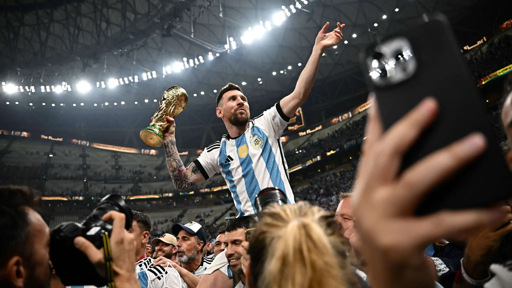 ليونيل ميسي يحتفل بفوز الأرجنتين بكأس العالم 2022 في قطر وسط حشد من الجماهير واللاعبين في ملعب مضاء.