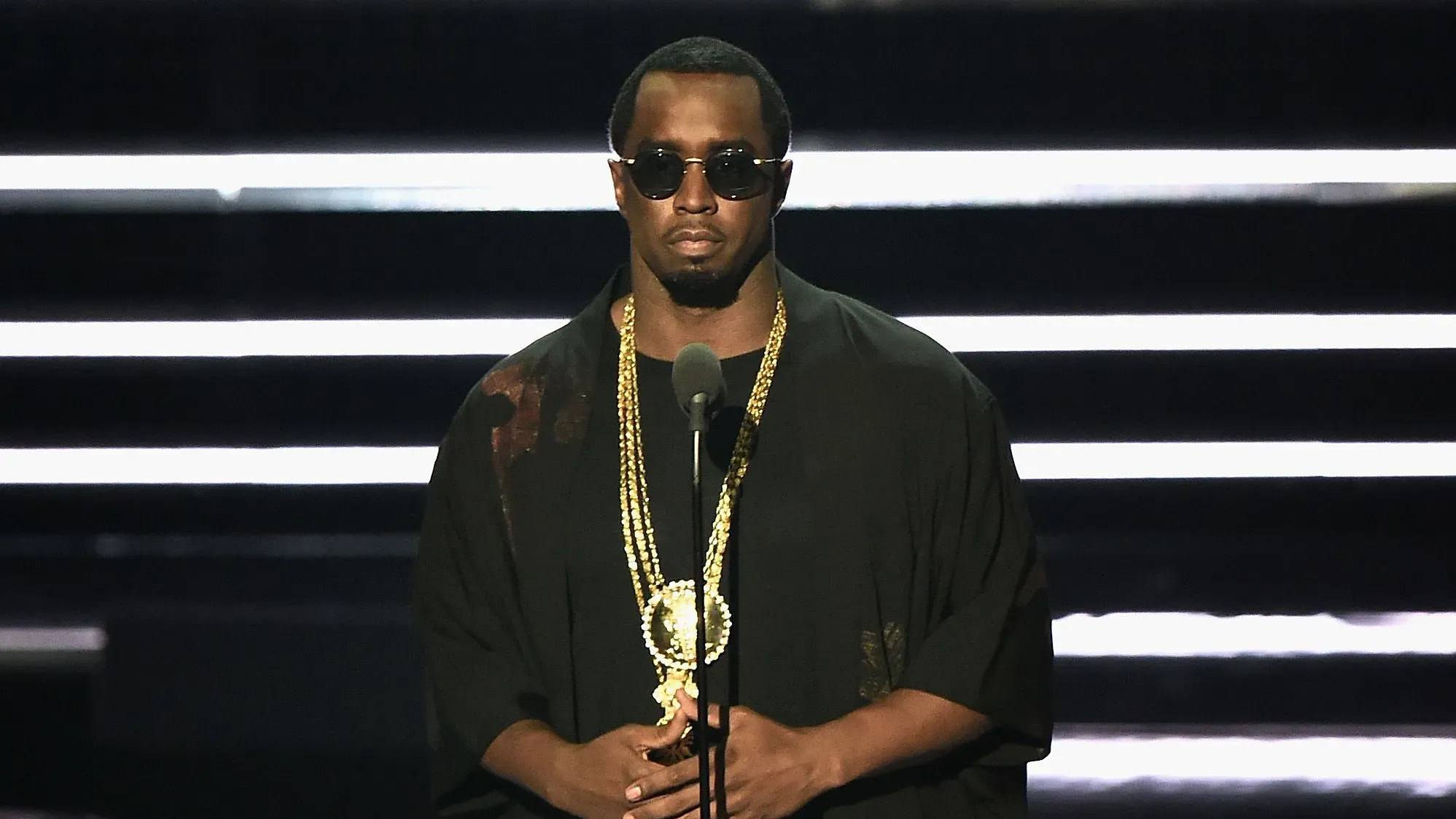 شون "ديدي" كومبس يقف على المسرح مرتديًا نظارات شمسية وسلسلة ذهبية، في سياق محاكمته المتعلقة بالاتجار بالجنس.